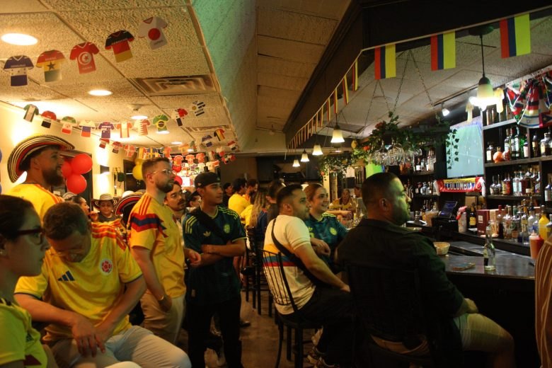 Crowded bar filled with fans in yellow jerseys, decorated with international flags and mini jerseys hanging from the ceiling.