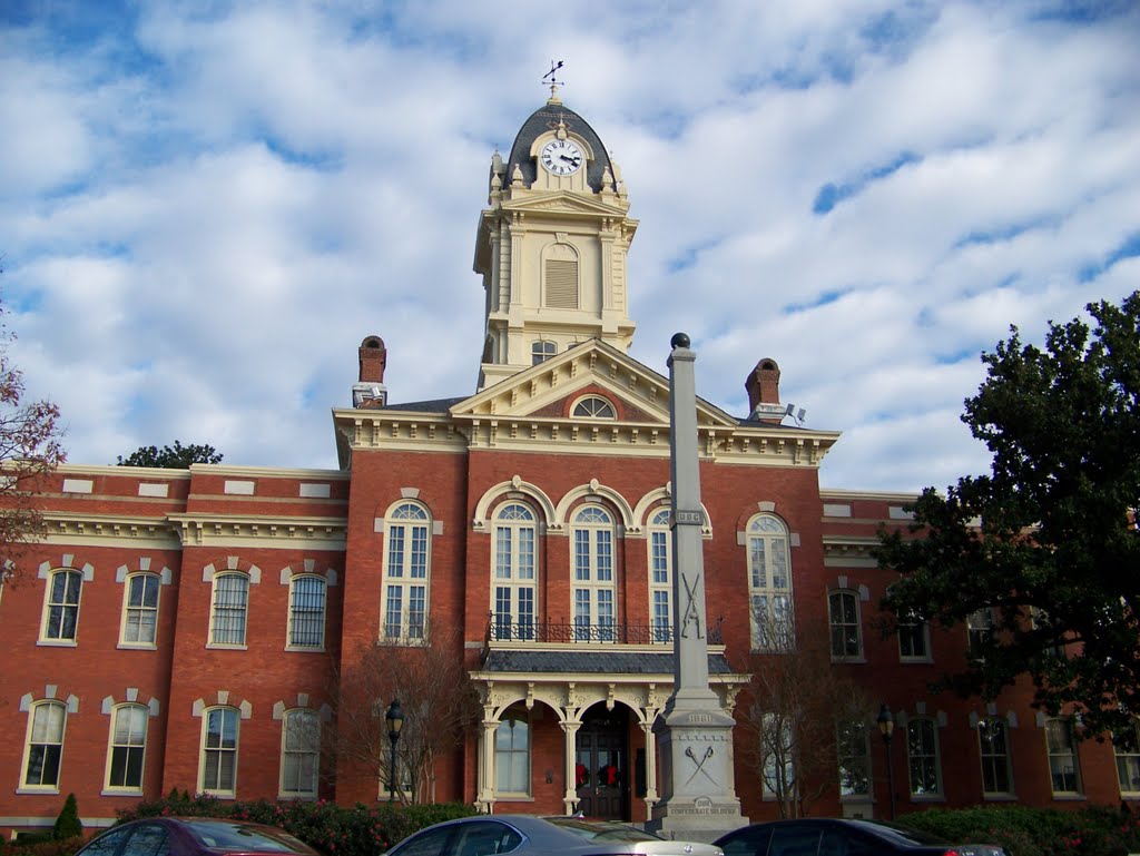 Historic red-brick courthouse with a clock tower, columned entrance, and obelisk monument.