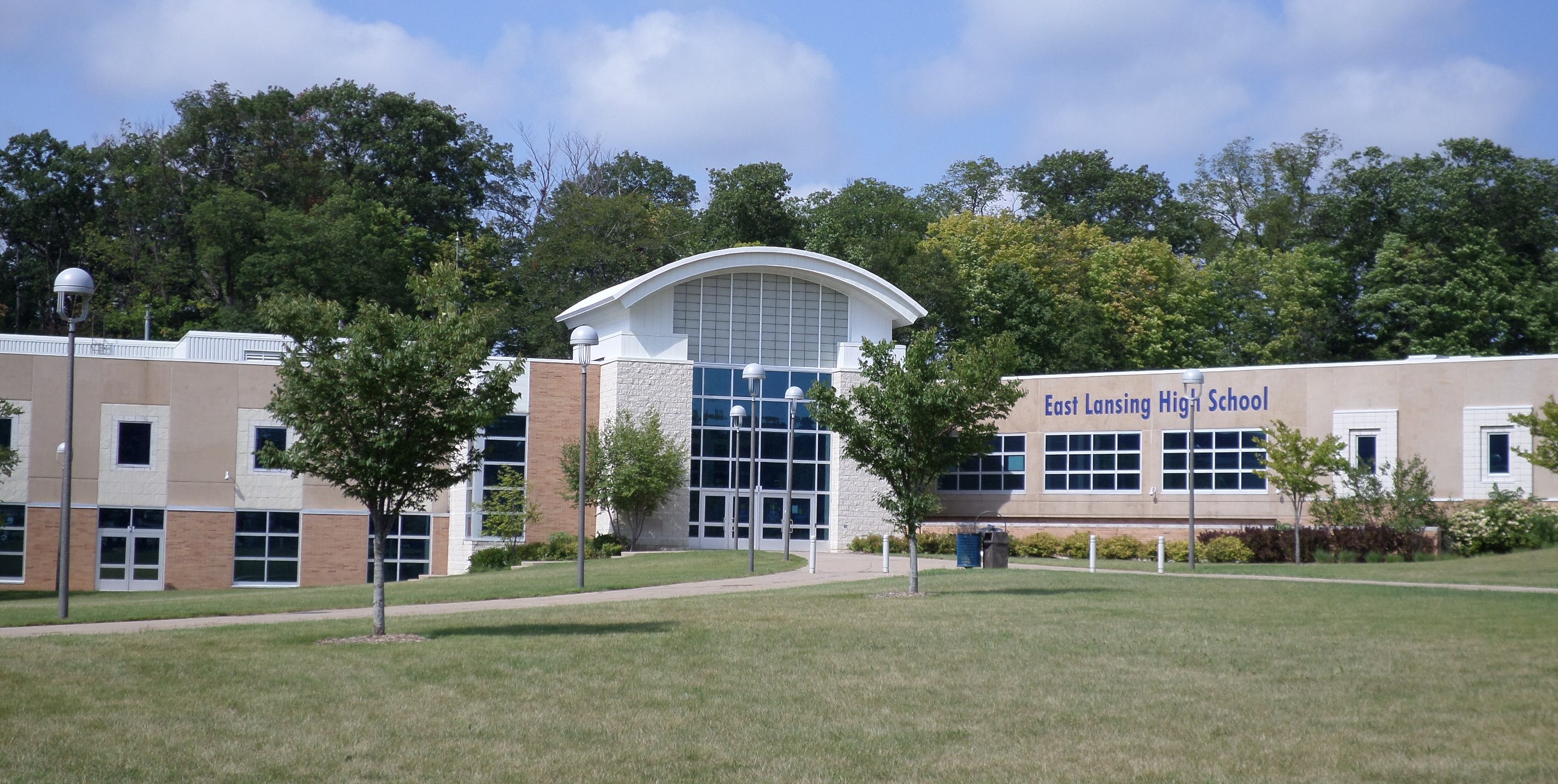 Exterior of East Lansing High School with curved entrance, blue glass panels, and school signage.