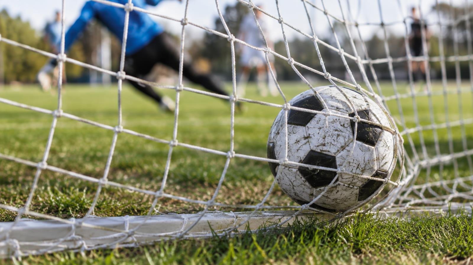 A soccer ball resting in the back of a goal net on a grass field.