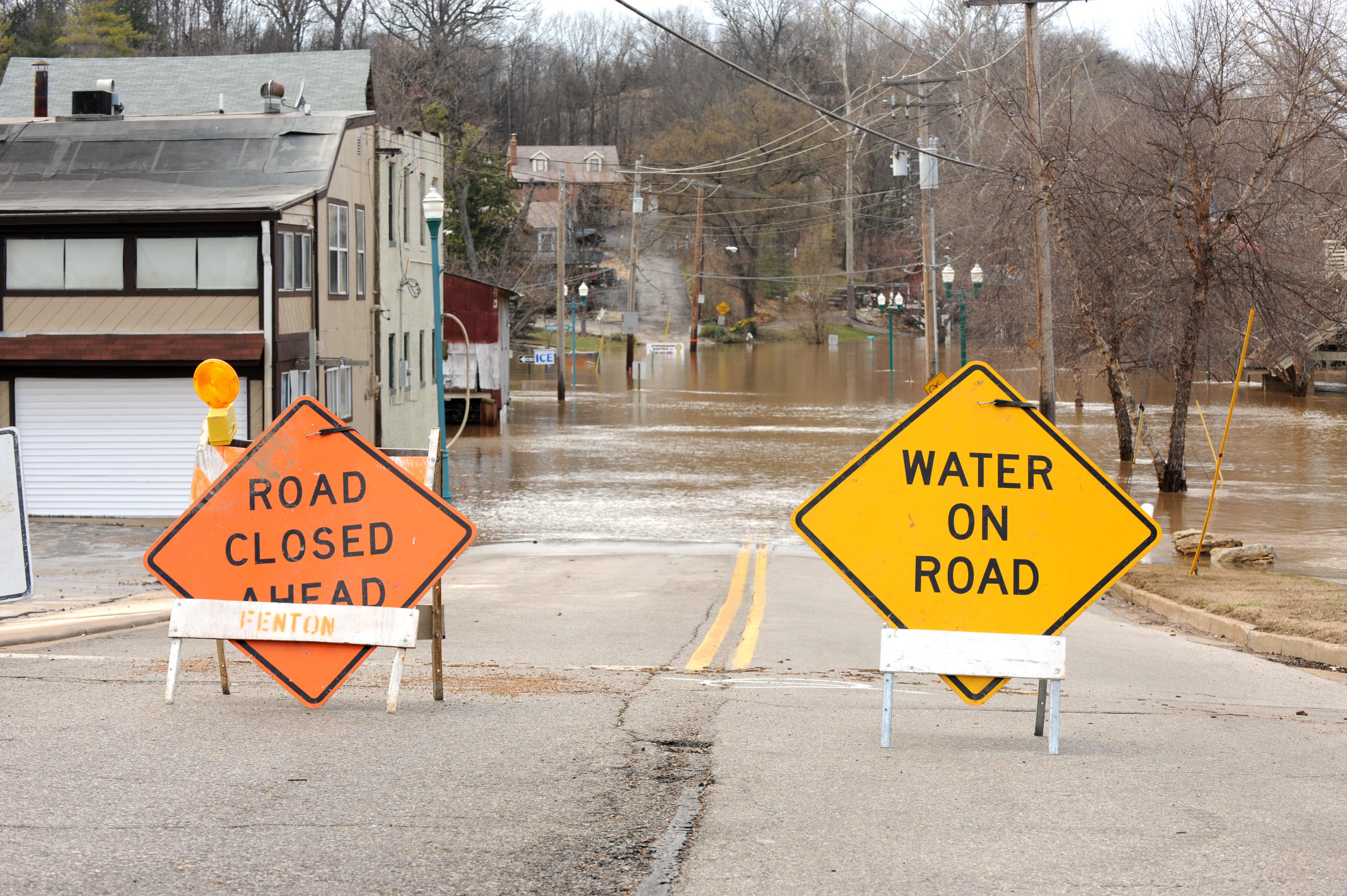 Road closed and water-on-road warning signs on a flooded neighborhood street.