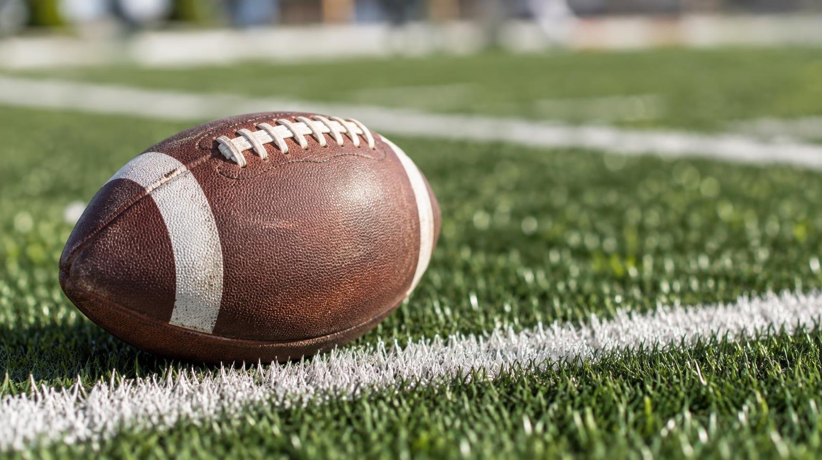 An American football resting on green artificial turf beside a white yard line.