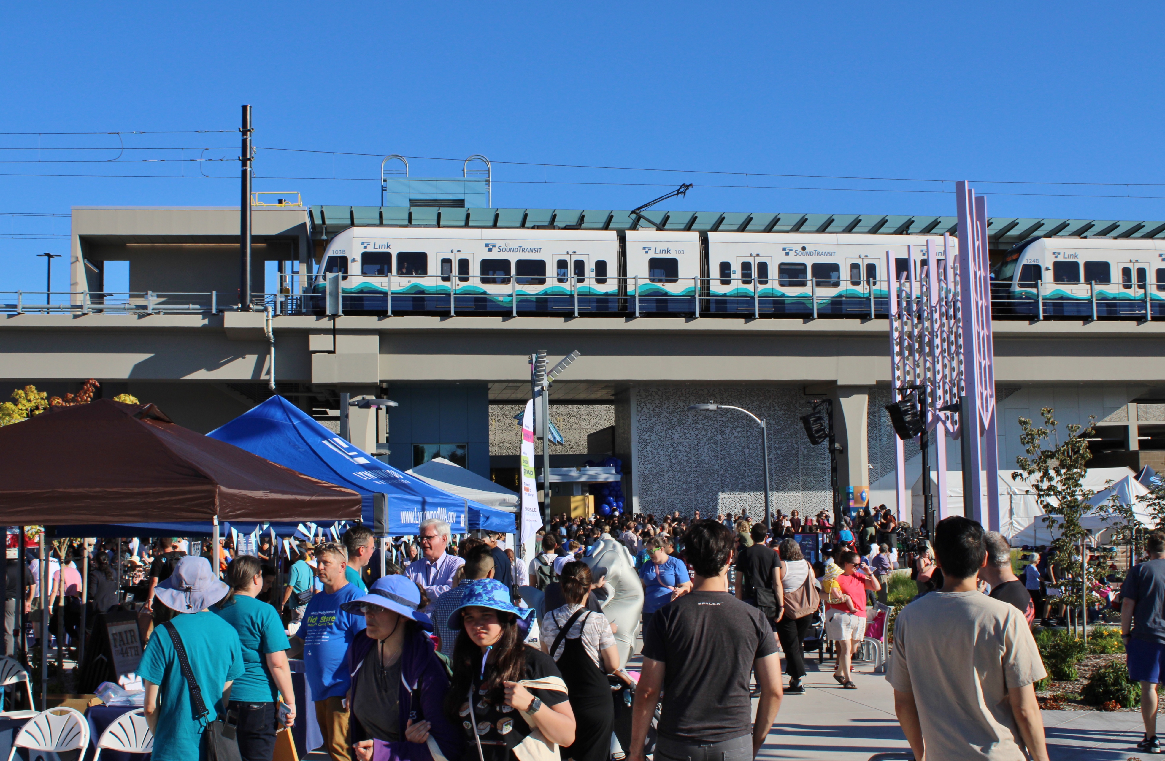 A light rail train on elevated tracks above a crowd gathered at street level.