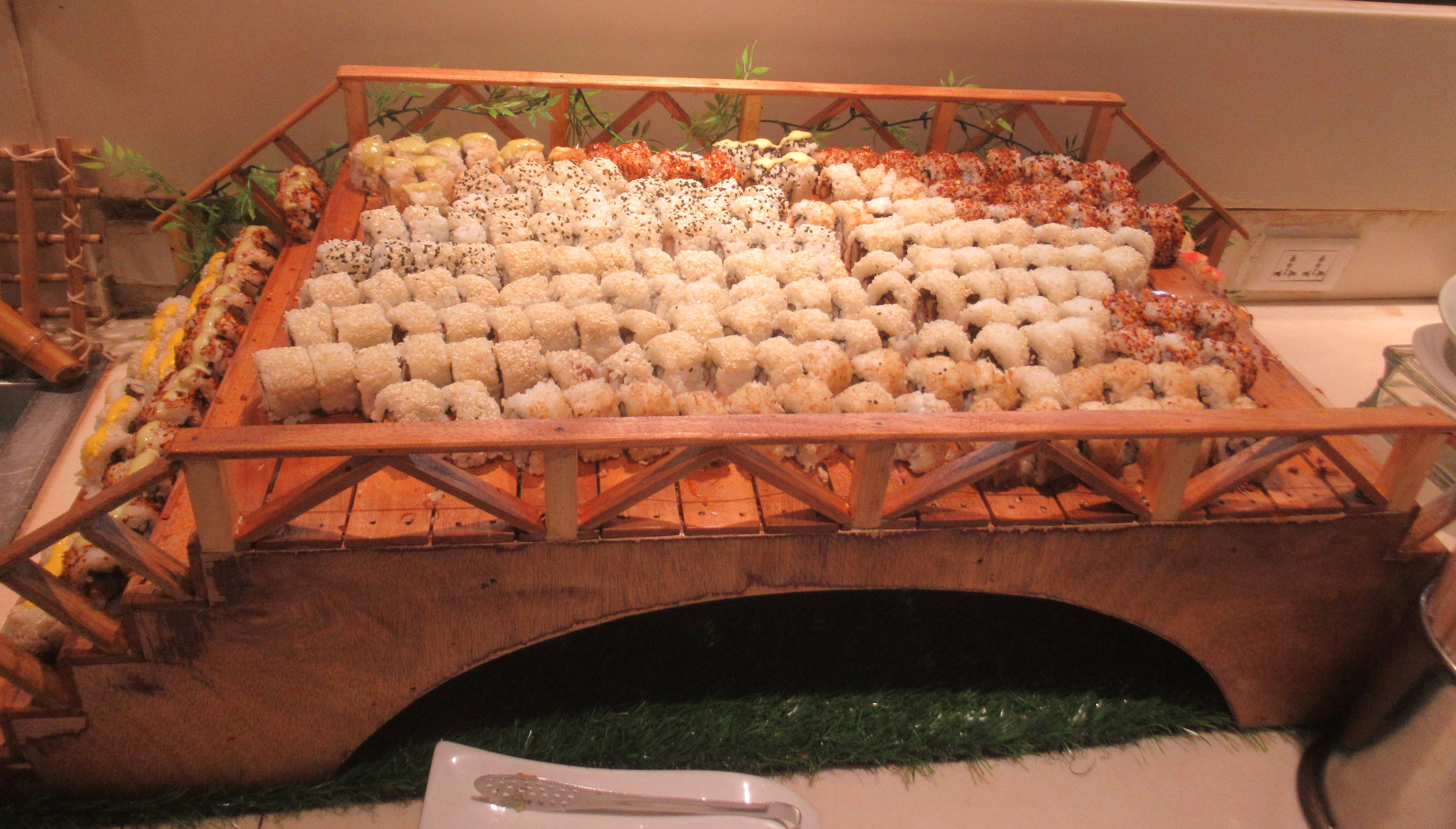 Dozens of assorted sushi rolls arranged in rows on a wooden bridge-shaped serving platter.