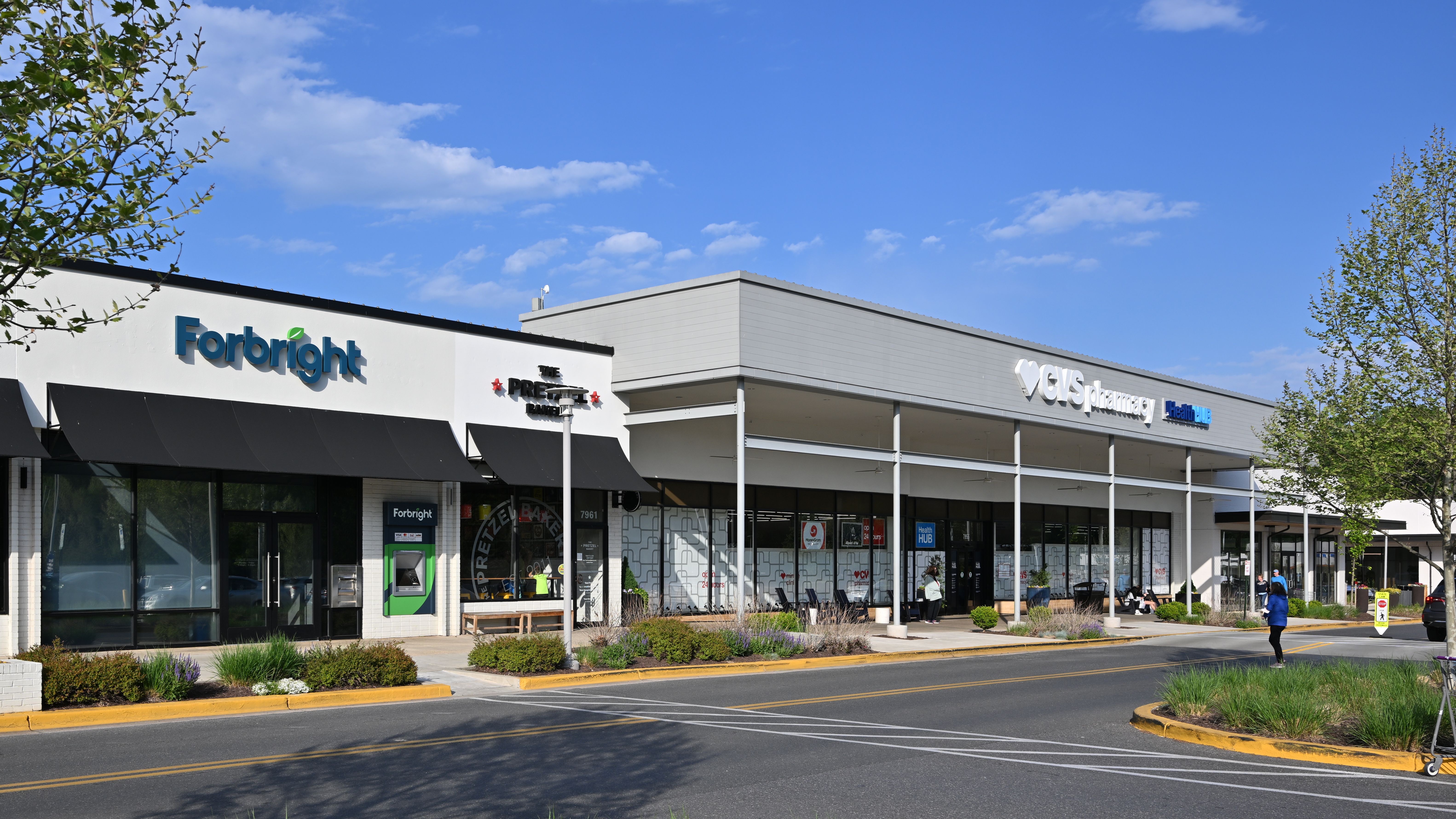 Strip mall exterior with retail storefronts and a parking lot in the foreground.