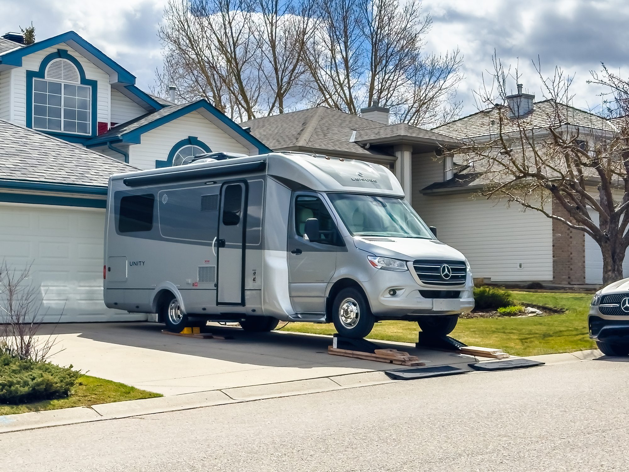 A silver Leisure Travel Vans Unity RV parked on a suburban driveway using leveling blocks.