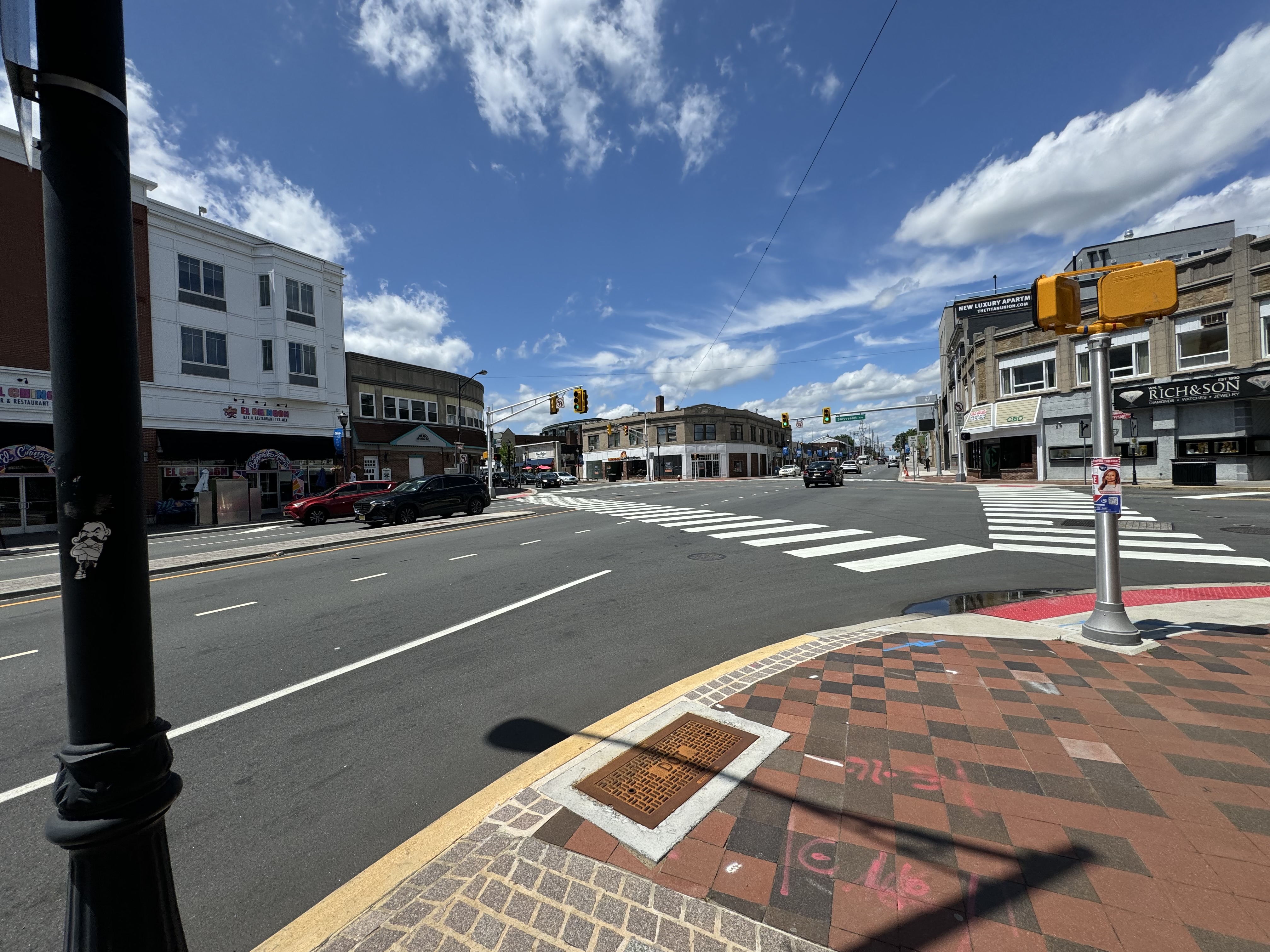 Downtown street intersection with storefronts and traffic signals on a partly cloudy day.