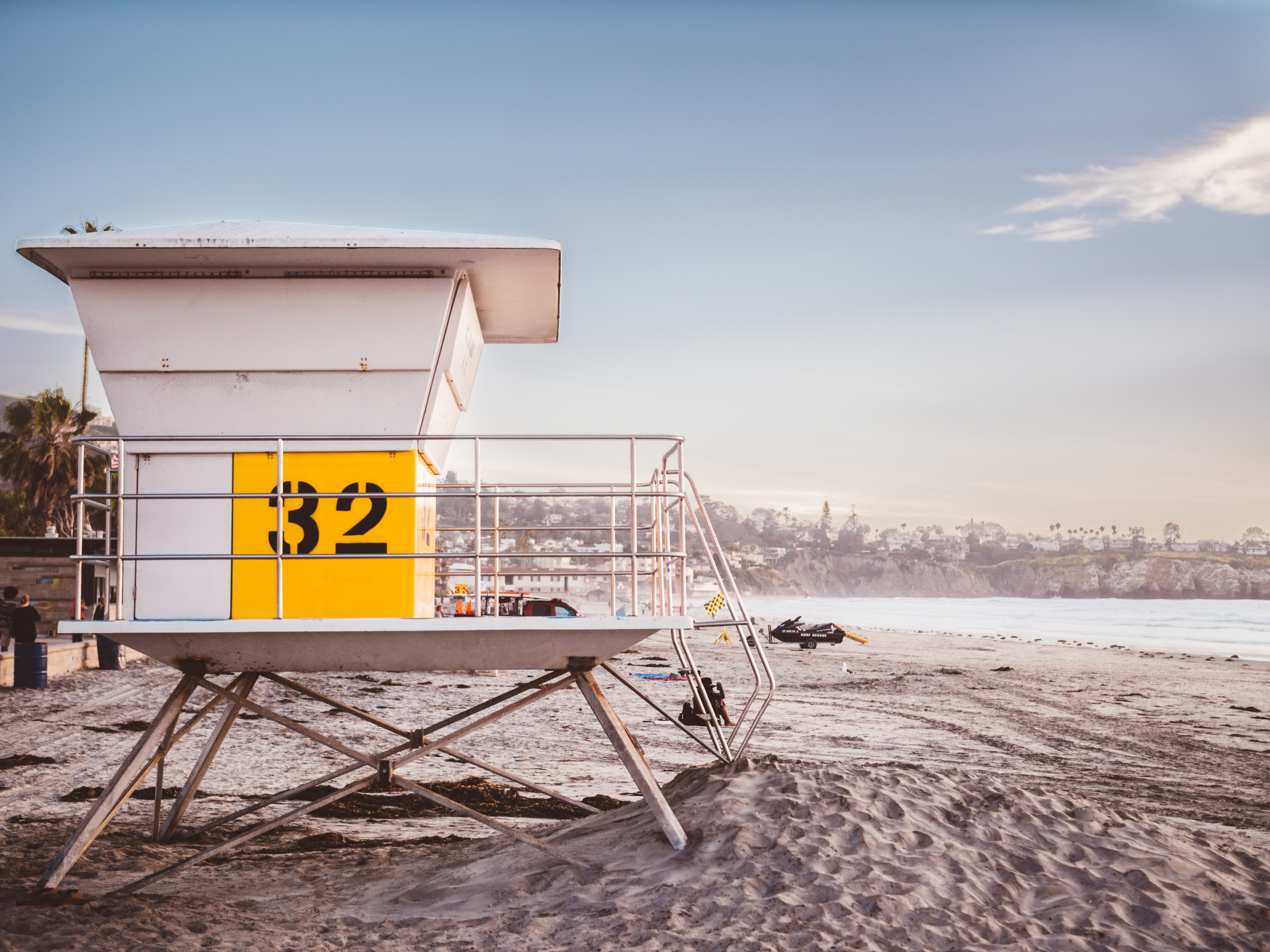 White lifeguard tower on an empty sandy beach with ocean and coastal hills behind it