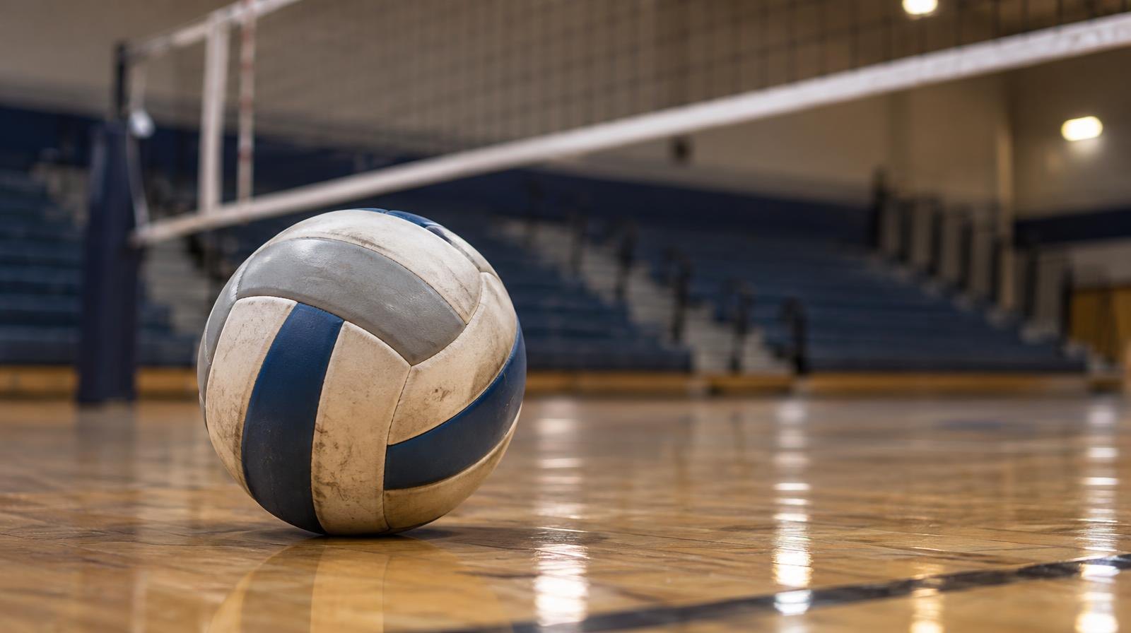 A volleyball resting on a hardwood gymnasium floor near a net.