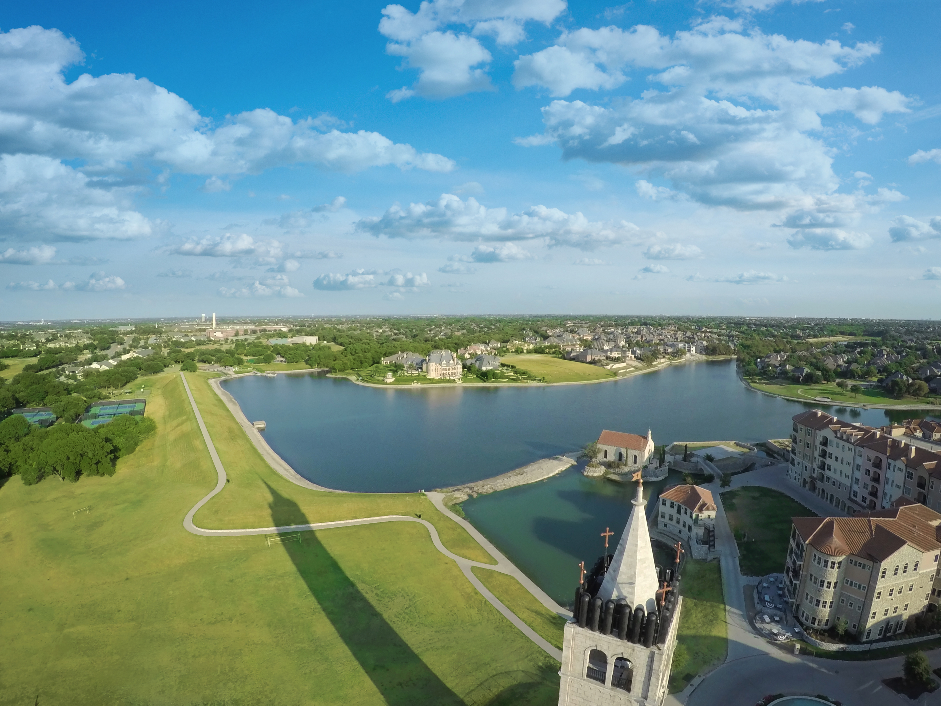 Aerial view of a lakeside mixed-use village with buildings, a steeple, and curved walkways