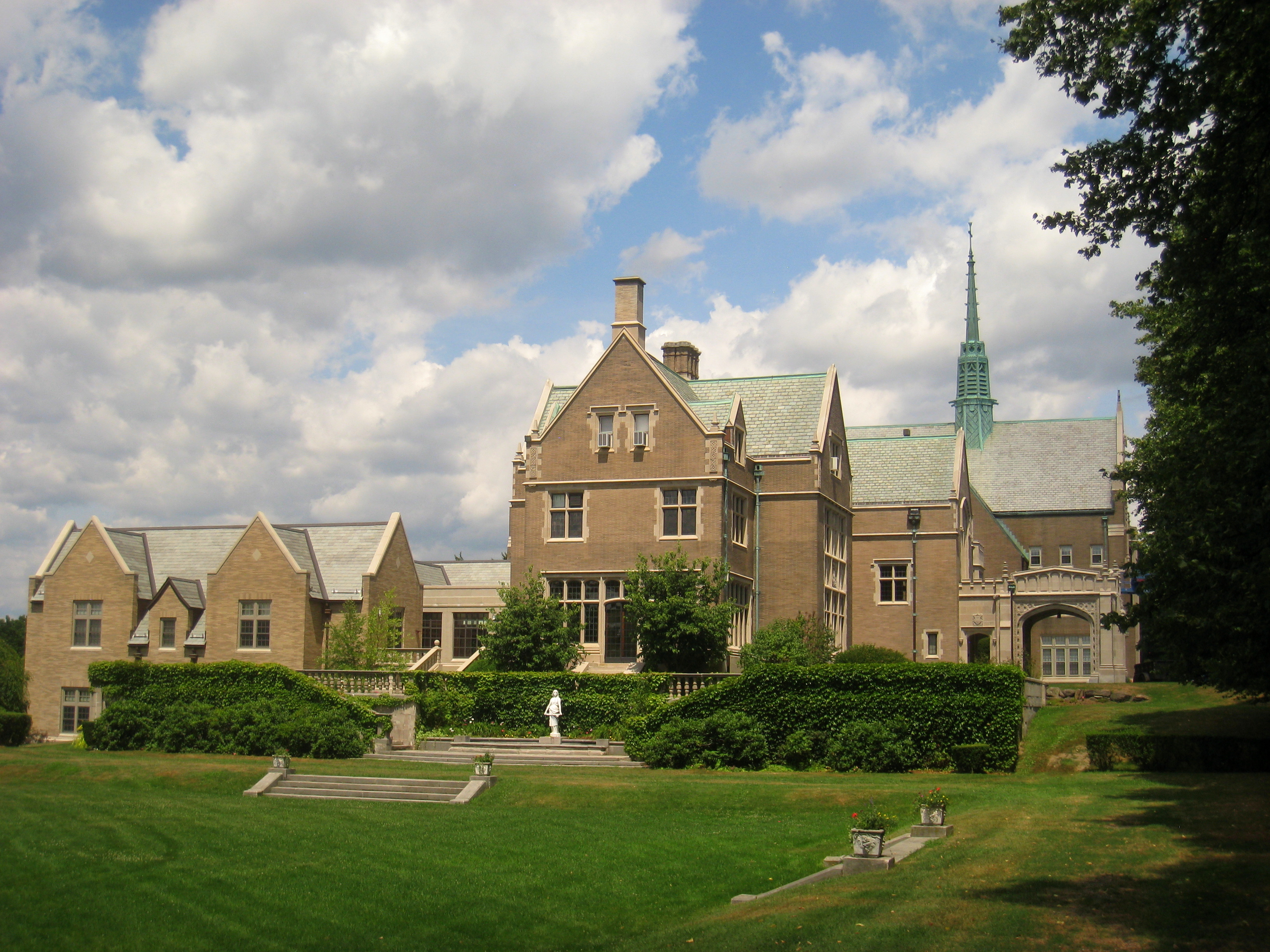 Stone Tudor Gothic school building with a chapel spire and manicured lawn.