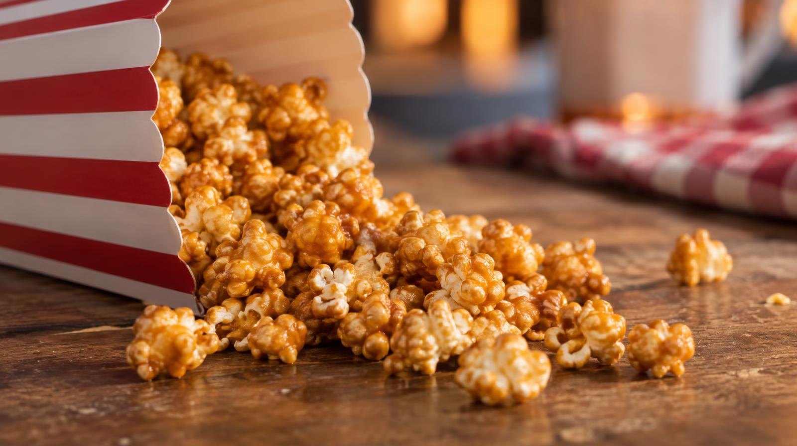 A striped paper box of caramel popcorn with golden kernels spilling out.