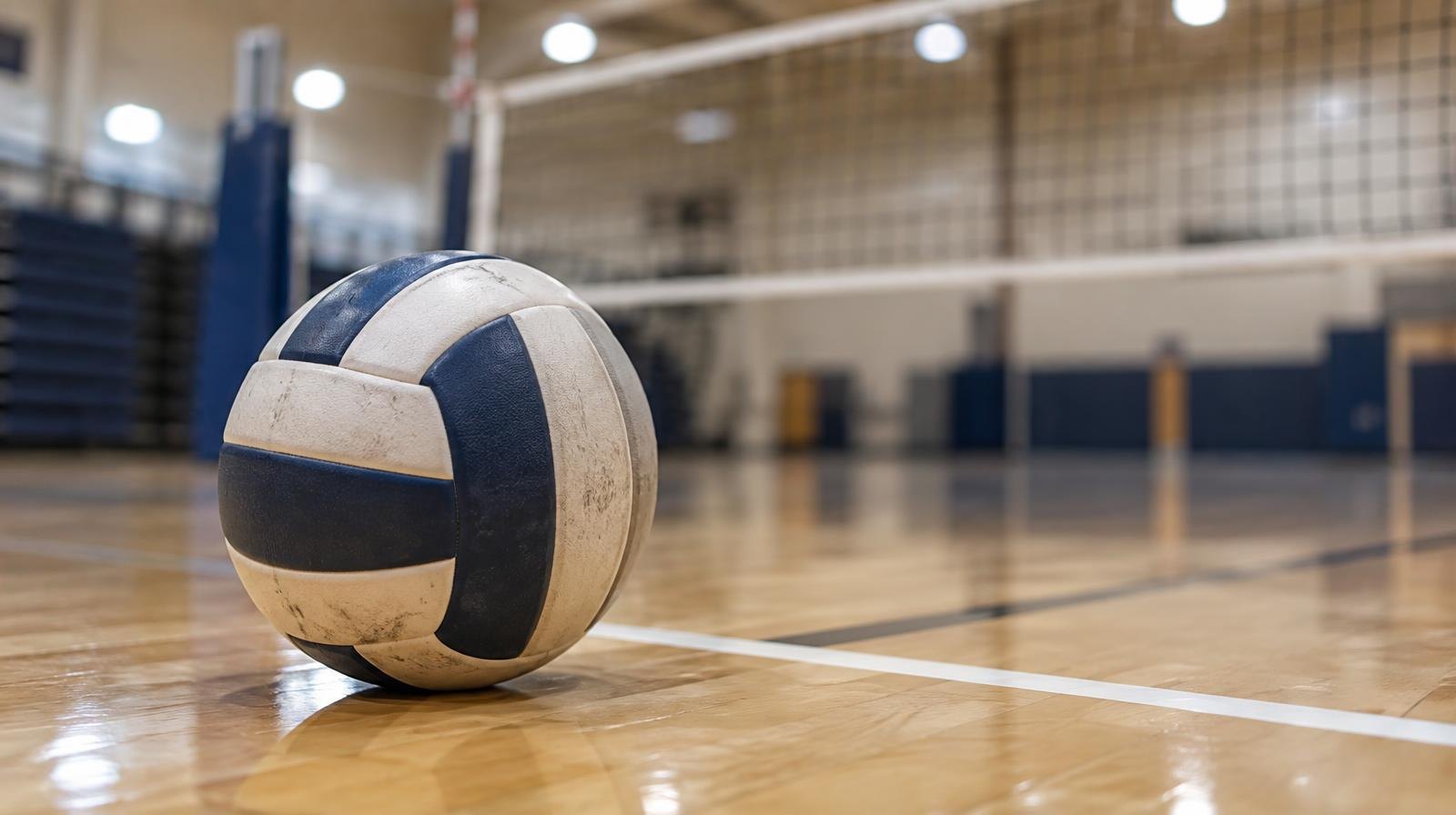 A volleyball resting on a hardwood gym floor near the net.