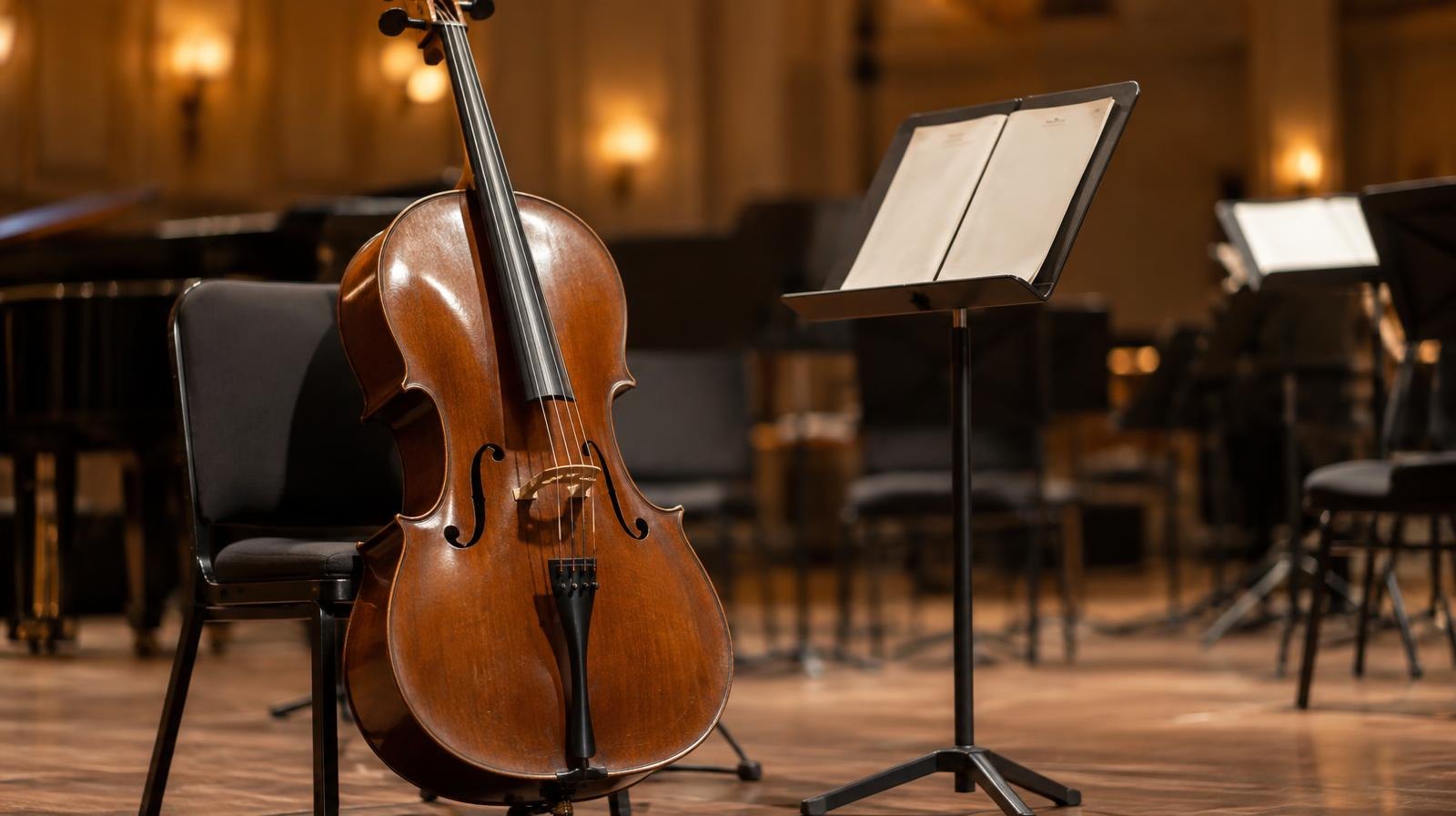 A cello stands upright on a stage next to an open music stand.