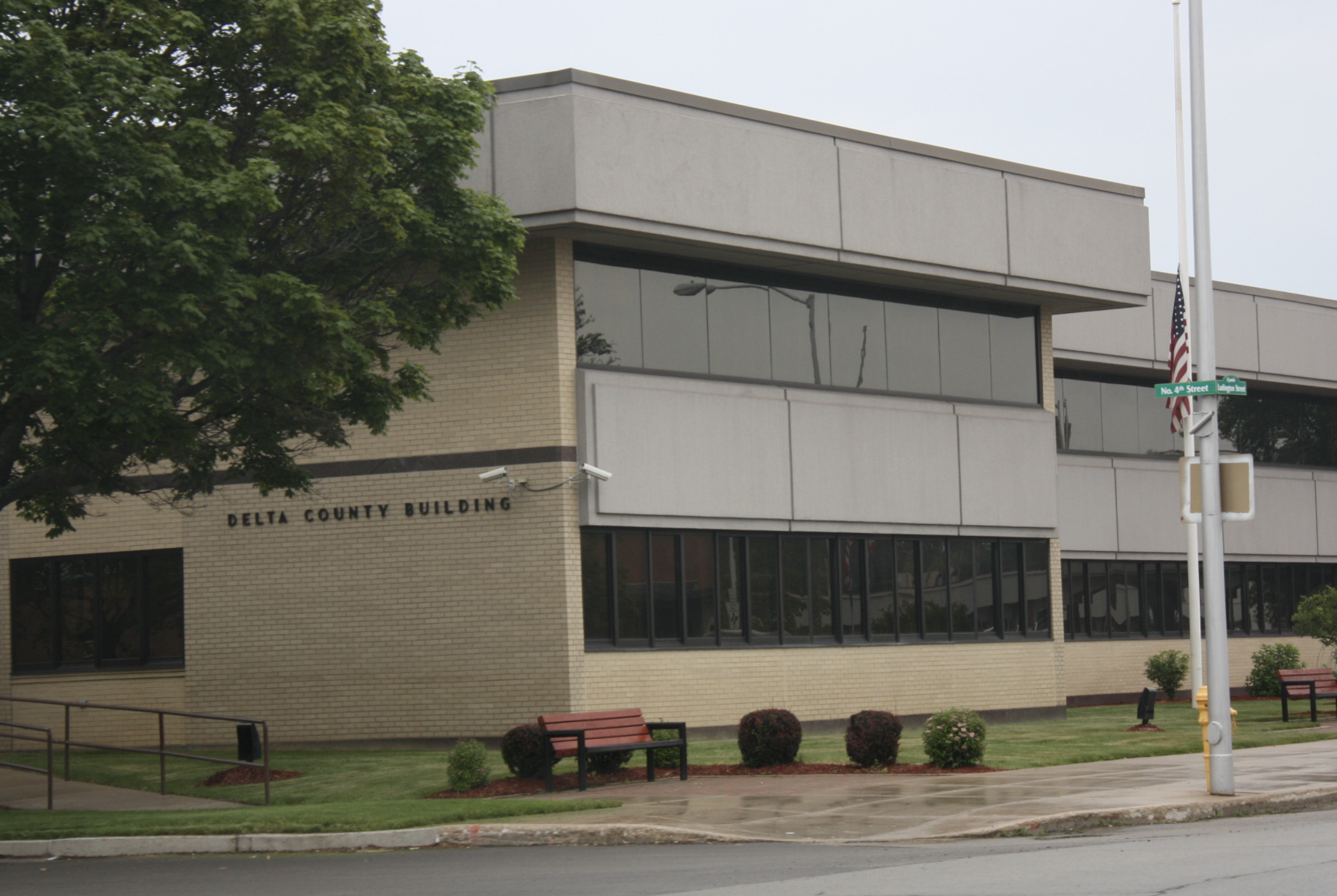 The Delta County Building in downtown Escanaba, Michigan, a two-story tan brick government building housing county offices and courts.