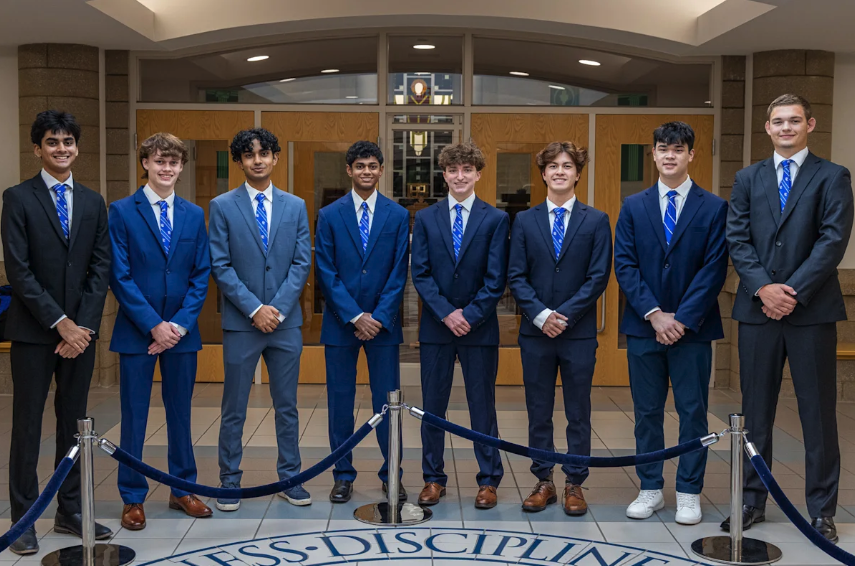 Eight Detroit Catholic Central High School seniors in suits stand together inside the school.