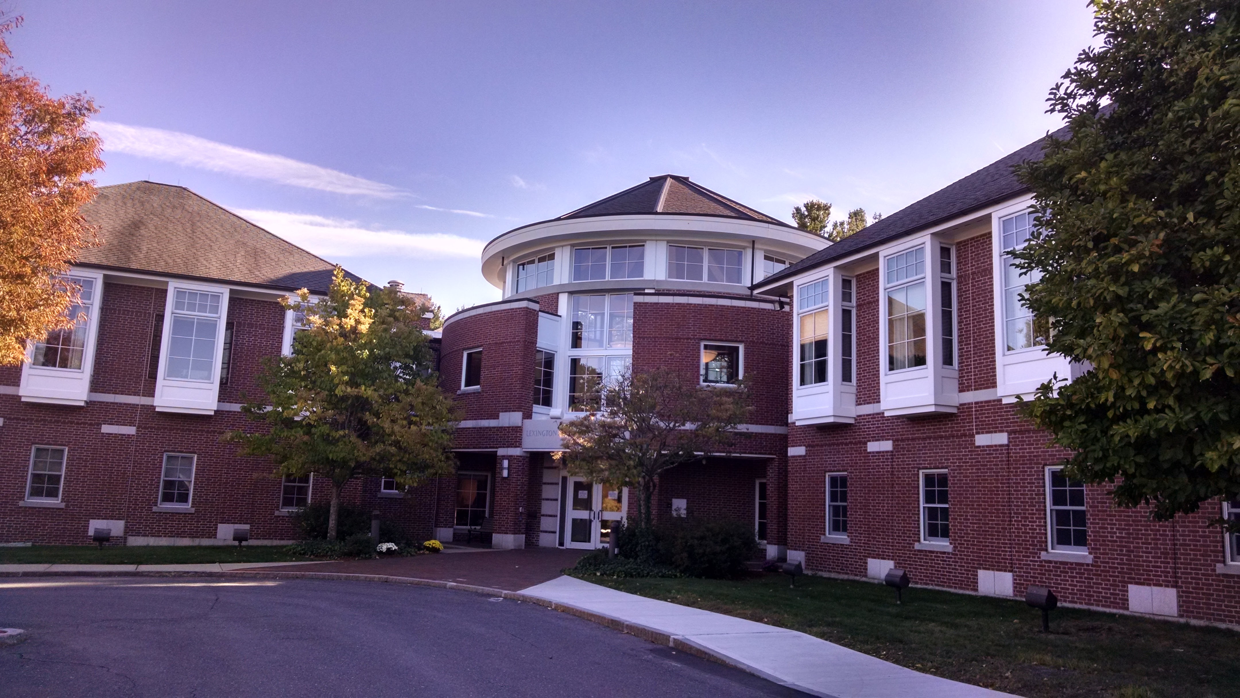 Two-story red brick community center with a circular glass rotunda entrance and autumn trees.