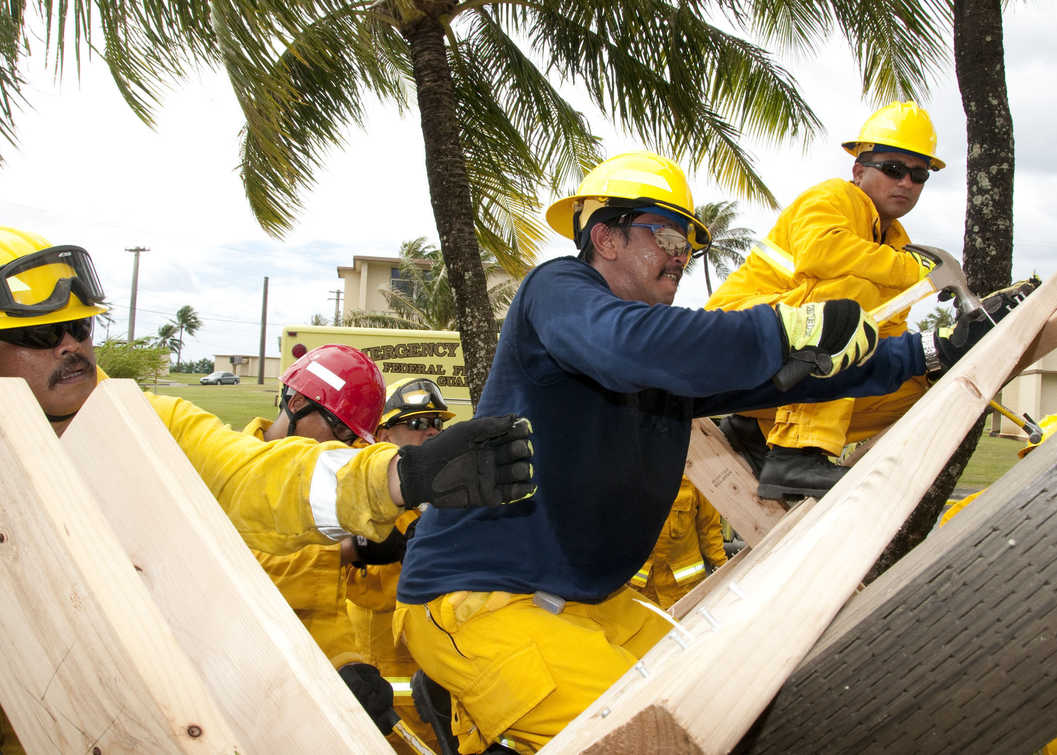 Firefighters in yellow gear and hard hats assemble wooden shoring during a training drill.