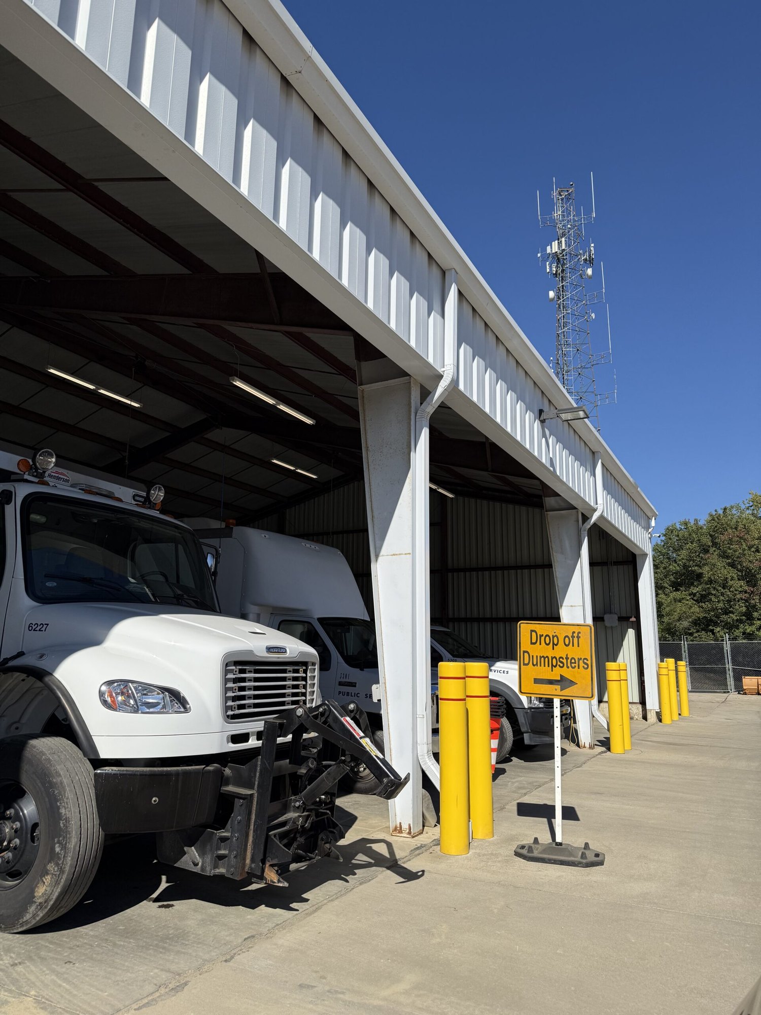 Open-bay municipal maintenance facility with a yellow drop-off dumpsters sign and a white truck parked inside.