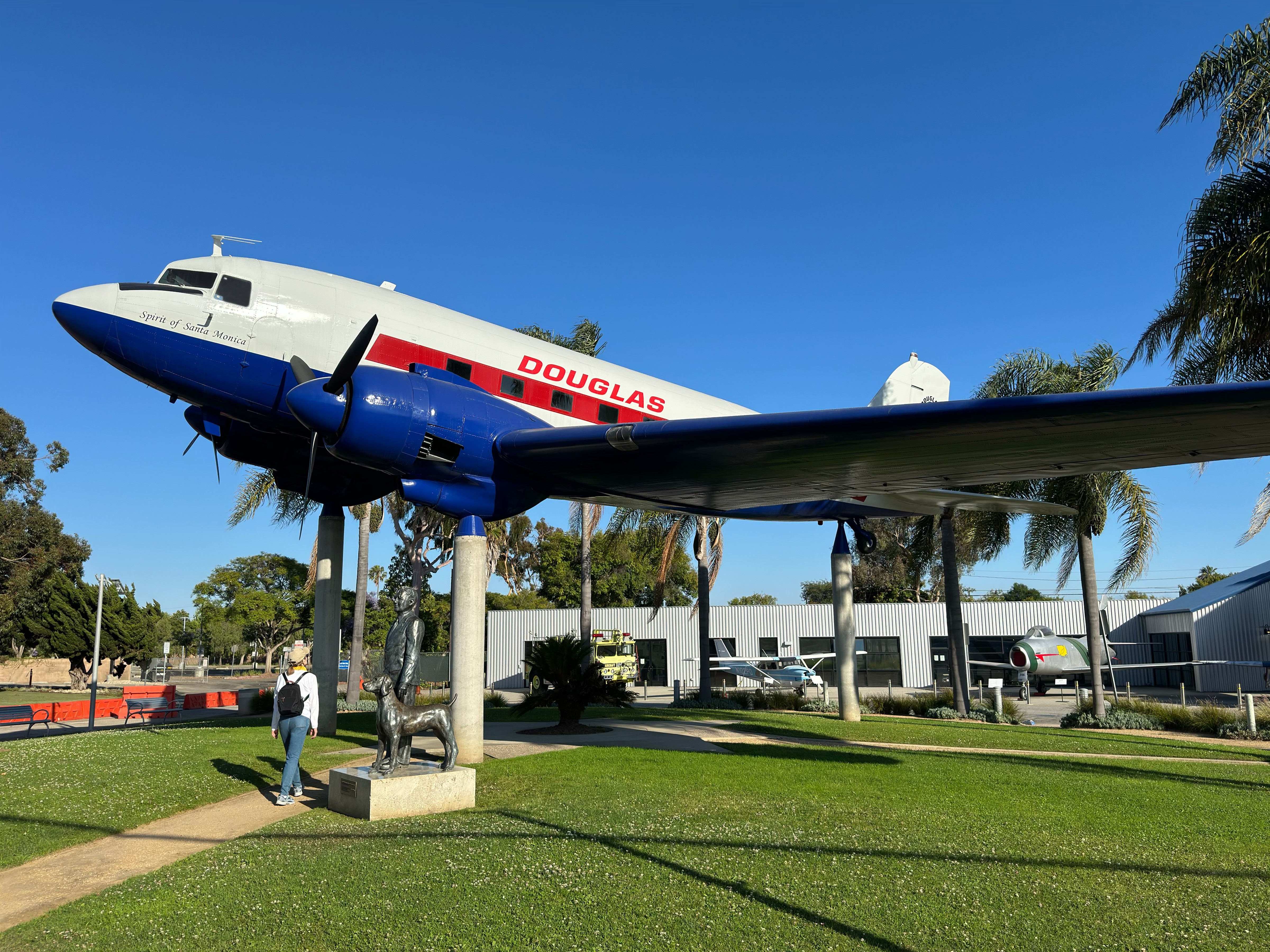 Restored Douglas DC-3 aircraft on outdoor pedestals at an airport, with palm trees and blue sky behind.