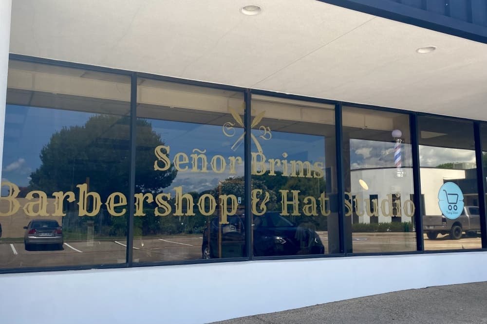 Storefront with gold lettering on dark tinted windows and a barber pole outside.