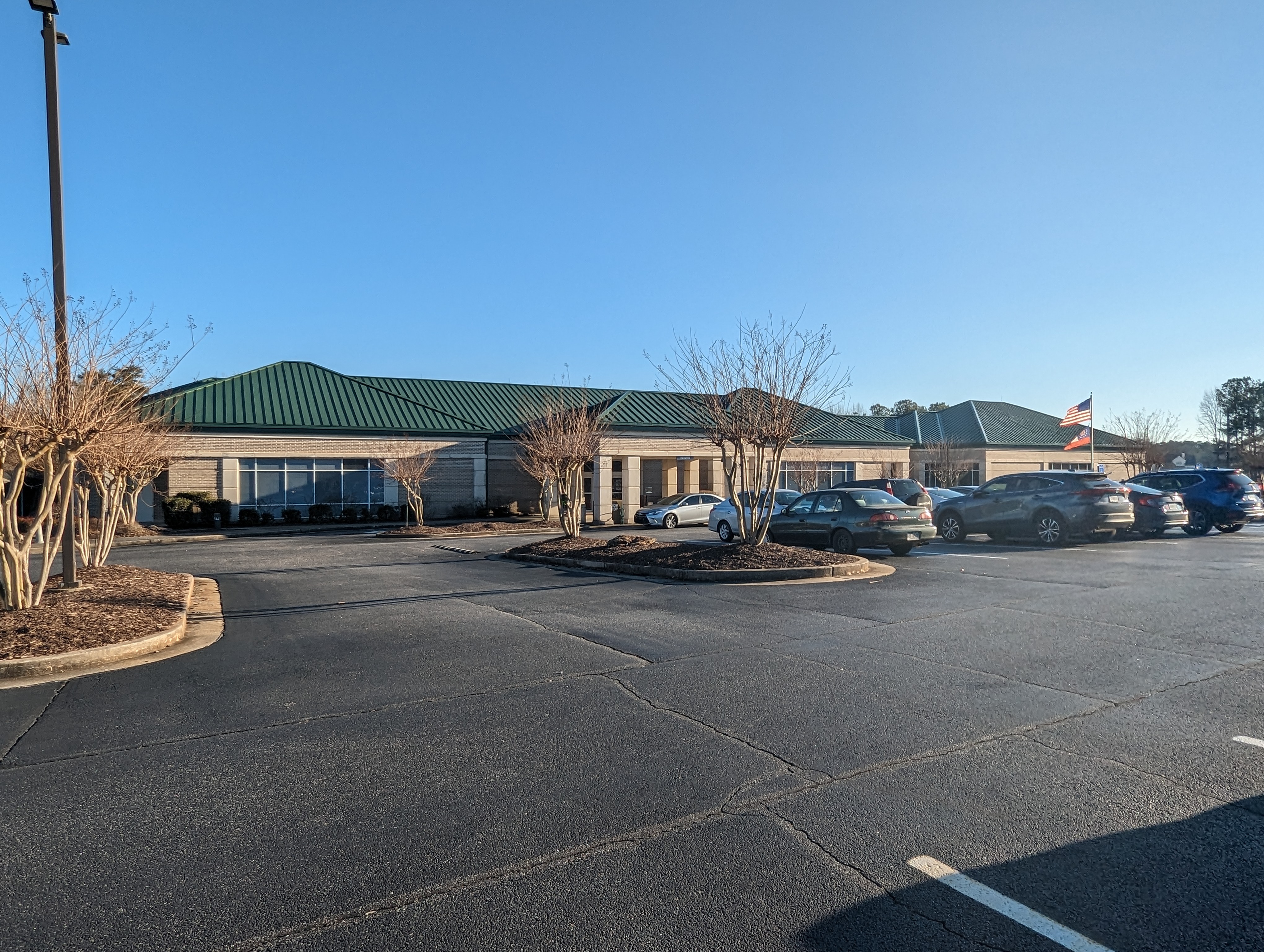 Single-story library building with a green metal roof and beige exterior under a blue sky.