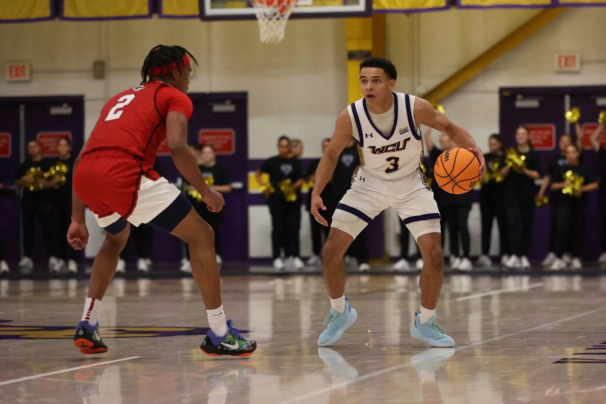 College basketball player in white number 3 jersey dribbles past a defender indoors.