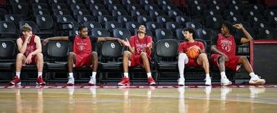 Five basketball players in red uniforms seated courtside at an indoor arena.