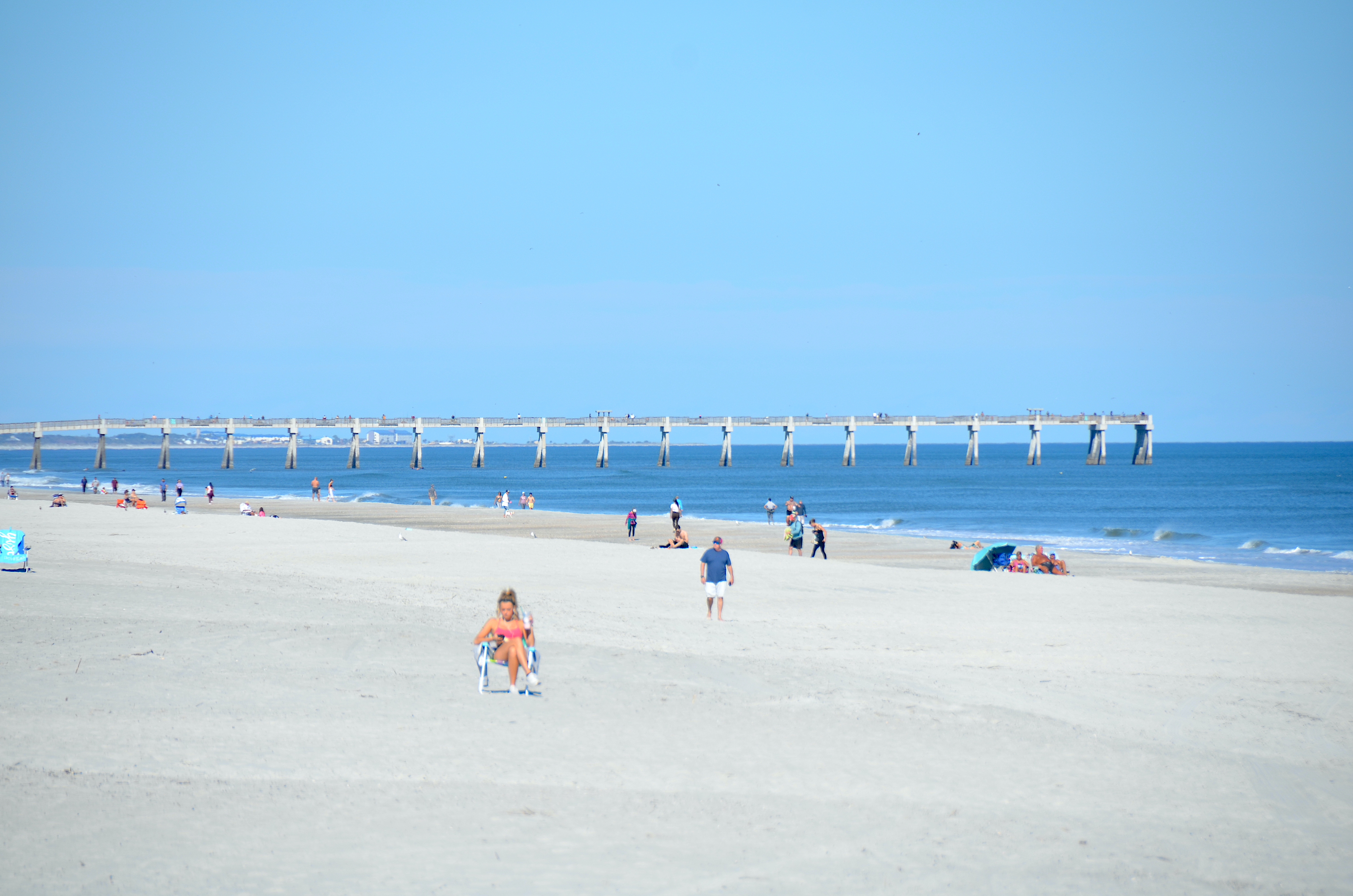 Sandy beach and long fishing pier extending into calm ocean water on a sunny day.