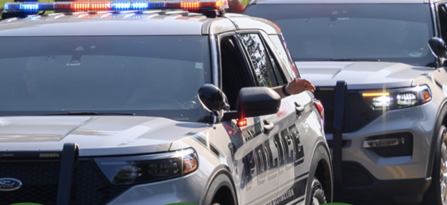 Two Dunwoody police SUVs with light bars activated parked close together at a scene, with an officer's arm visible out the driver's window.