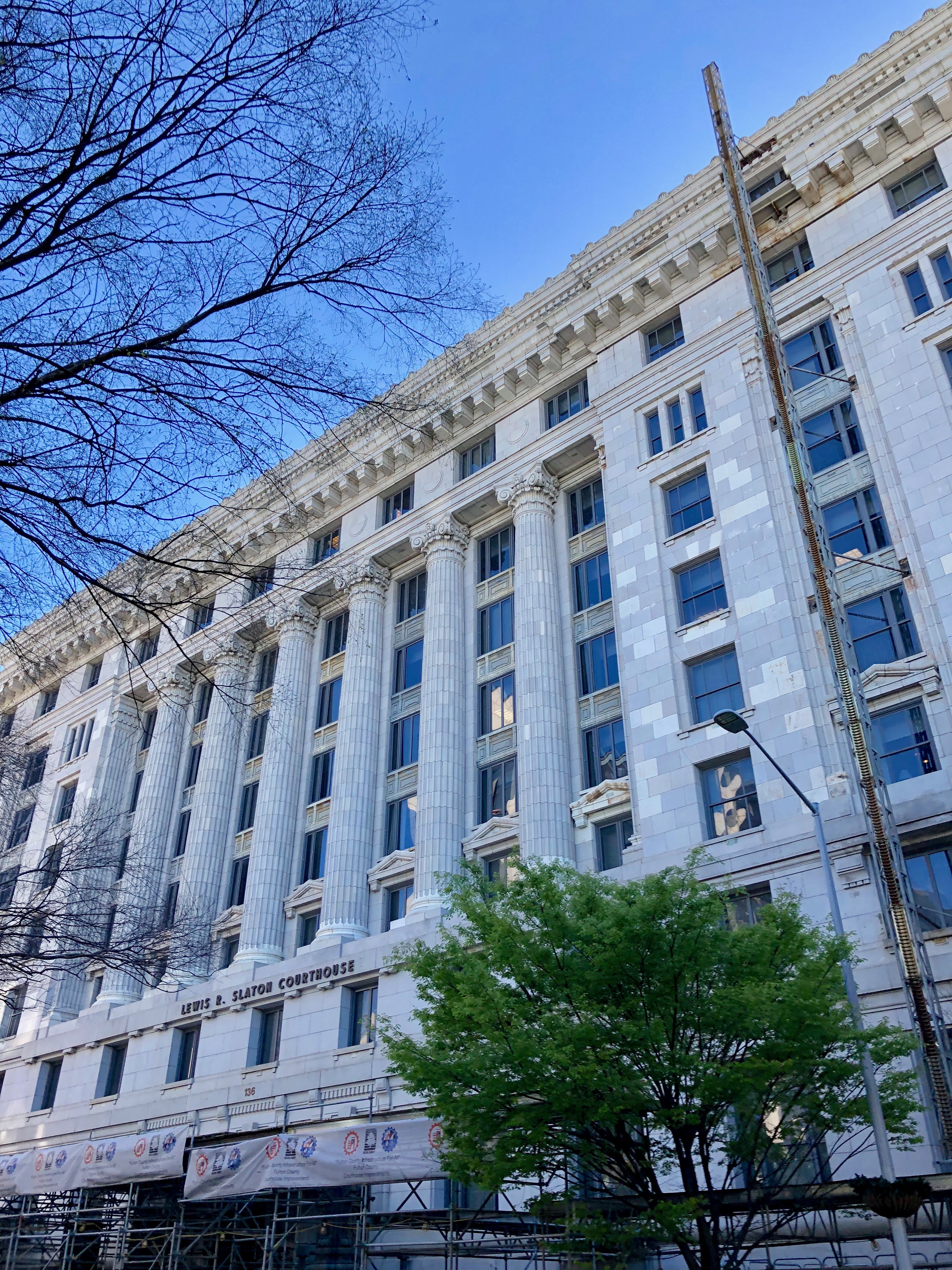 Neoclassical courthouse with tall columns and scaffolding, framed by trees.
