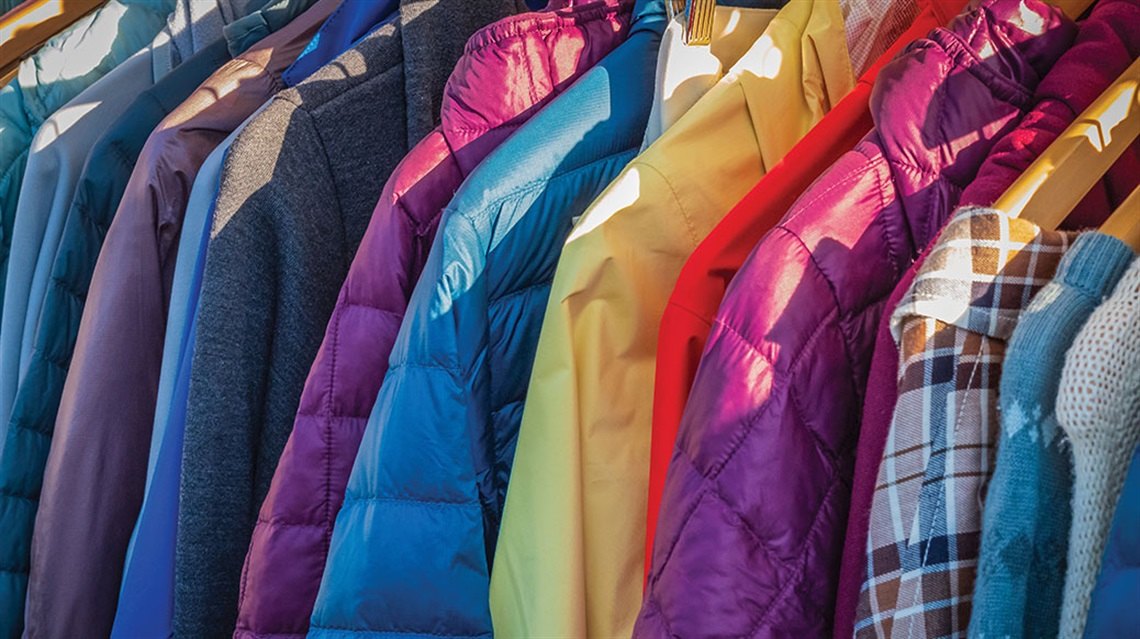 Colorful coats and jackets hanging closely together on a clothing rack.