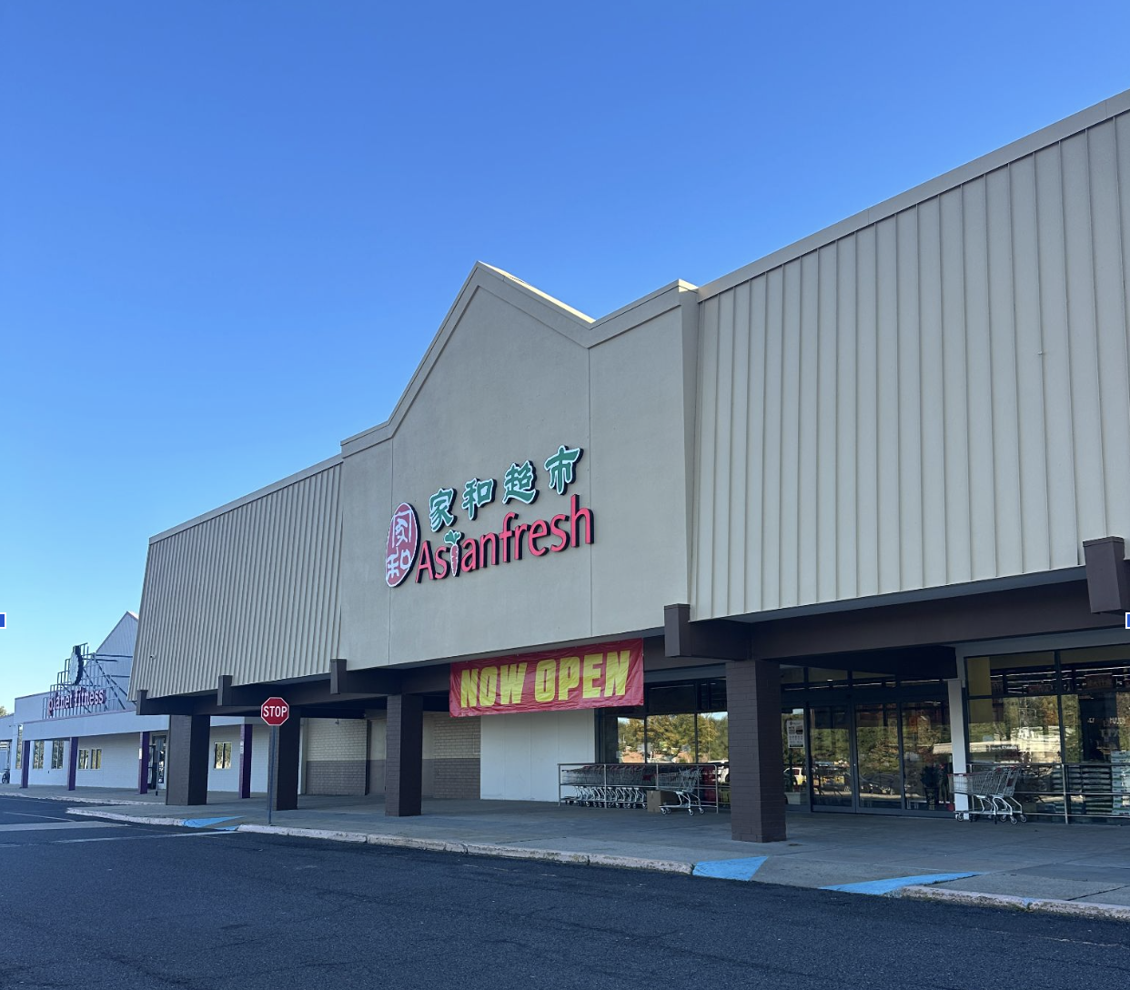 Exterior of a large retail grocery store with English and Chinese signage and a pink Now Open banner.