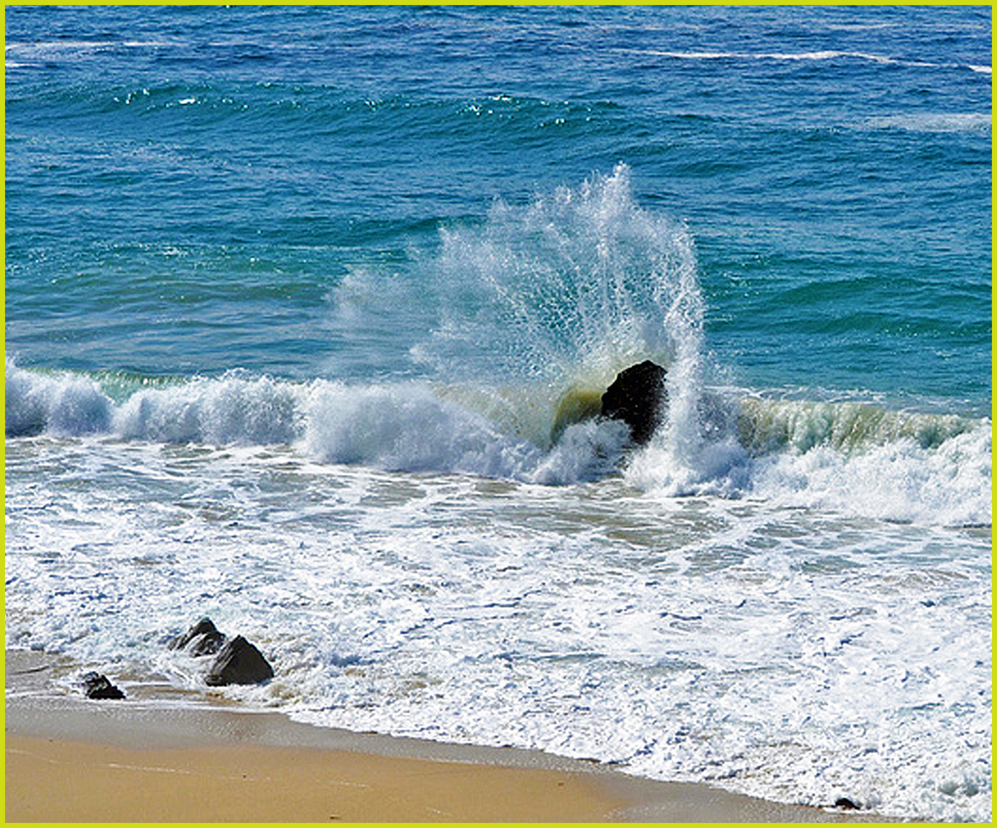 Waves crashing against dark rocks on a sandy beach with white sea spray