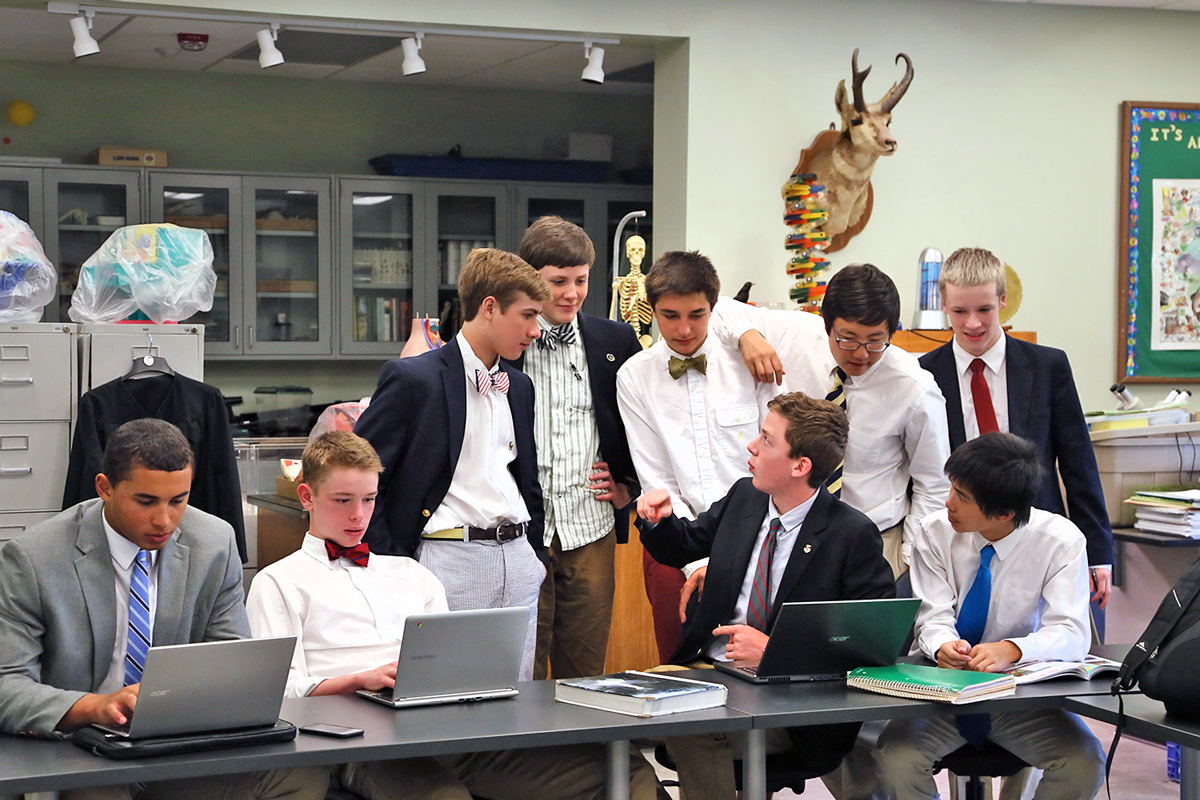 Group of students gathered around open laptops in a school classroom.