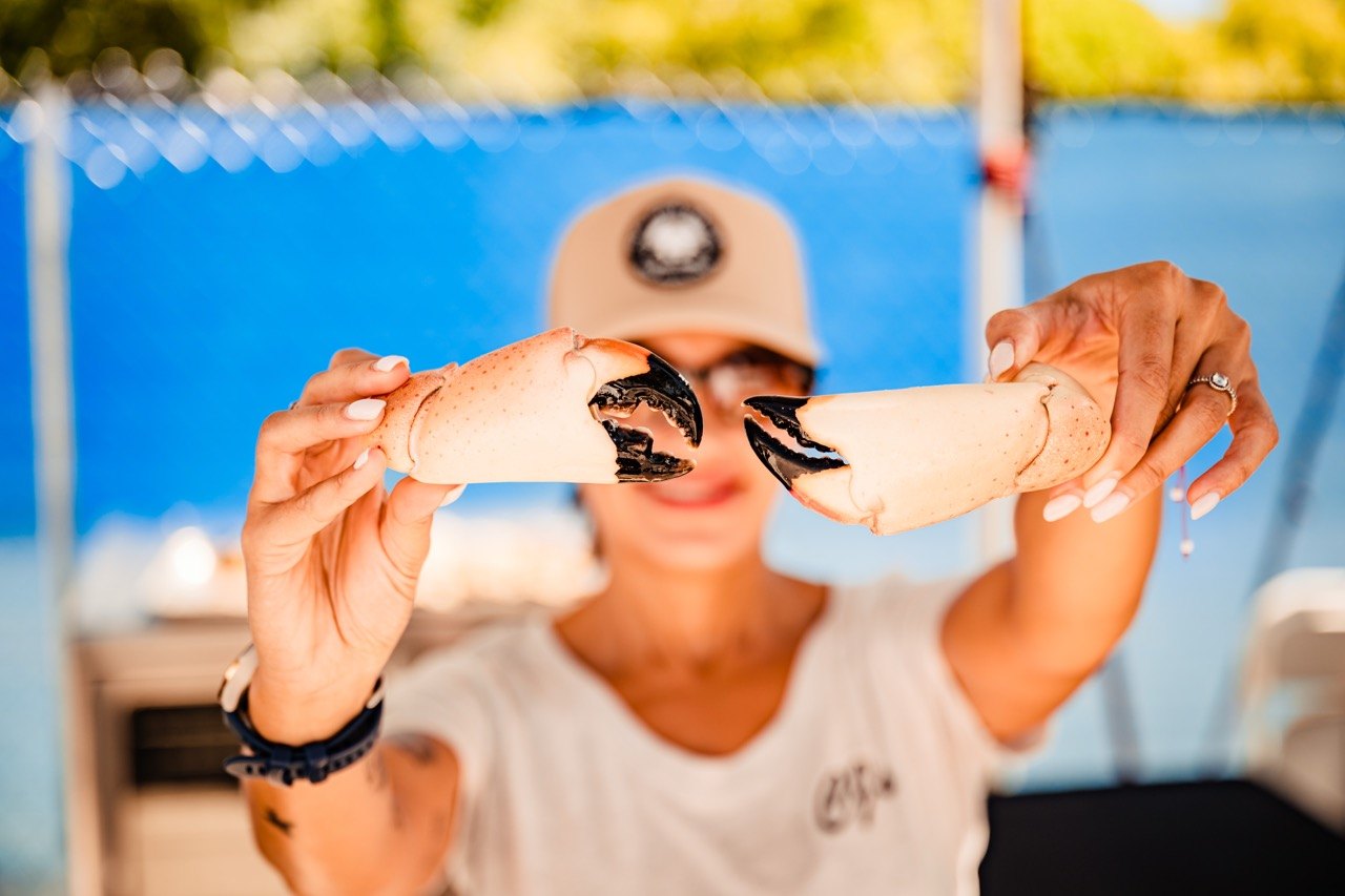 A woman holds two split stone crab claws up toward the camera outdoors.