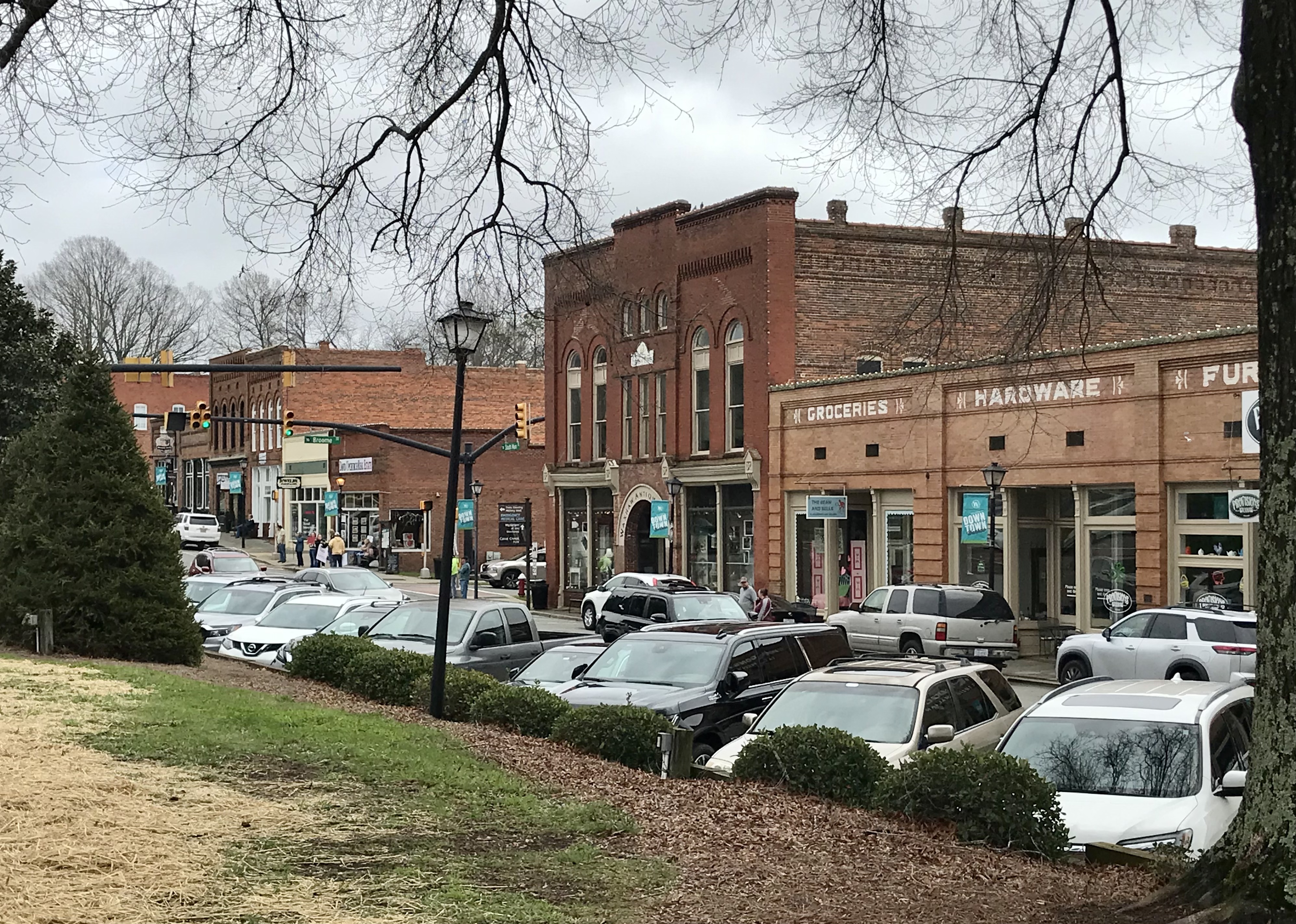 Brick commercial storefronts along a small-town main street with parked cars.