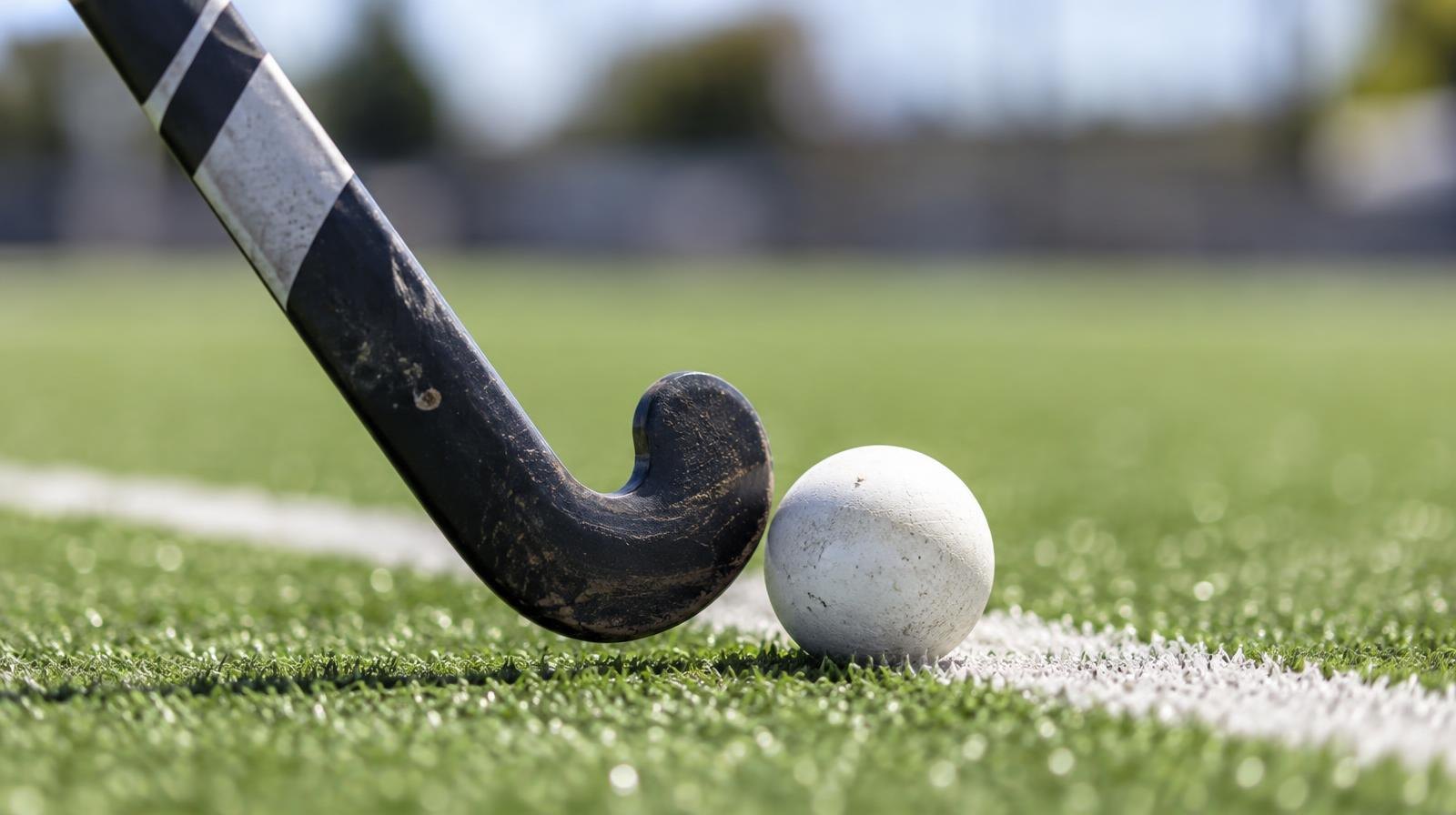 A field hockey stick and ball resting on green artificial turf beside a white line.
