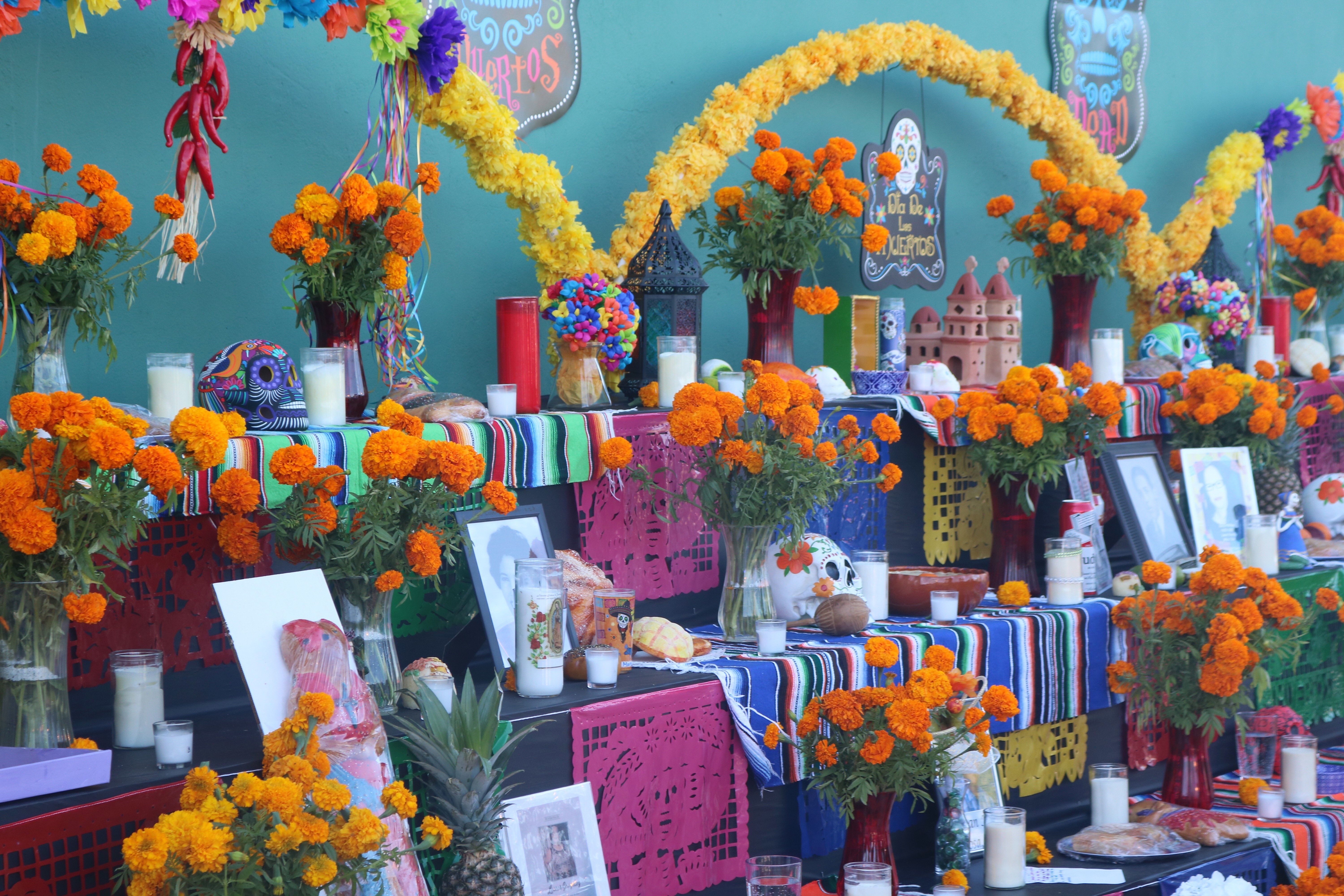 Colorful multi-tiered ofrenda altar decorated with orange marigolds, candles, and photographs.