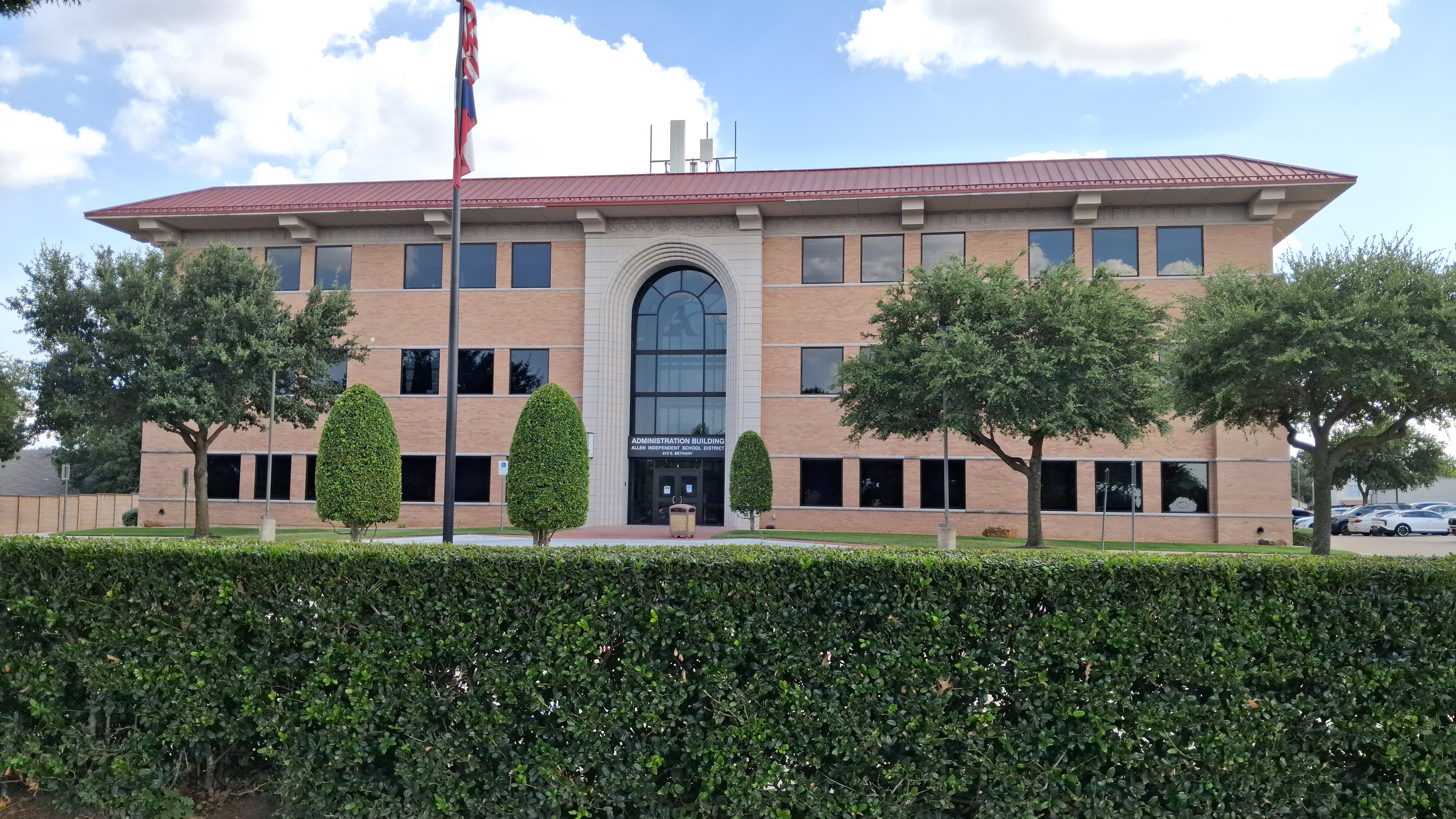 Two-story tan brick school administration building with red tile roof and arched entrance.