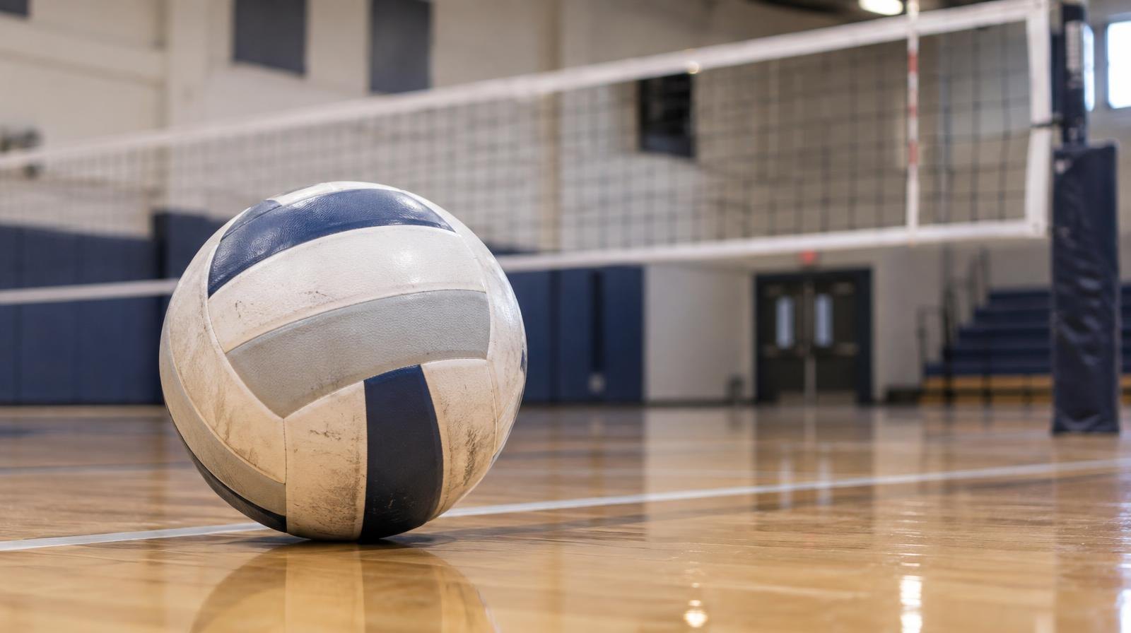 A volleyball resting on a hardwood gymnasium floor near the net.