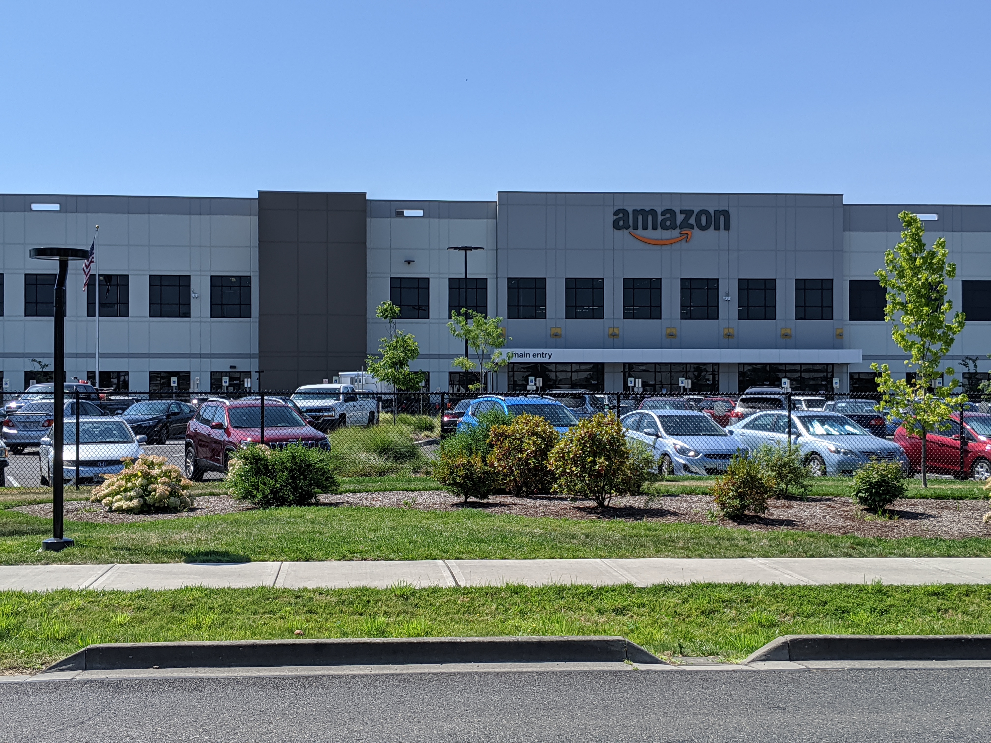 Amazon warehouse building with large parking lot and Amazon logo on the facade.
