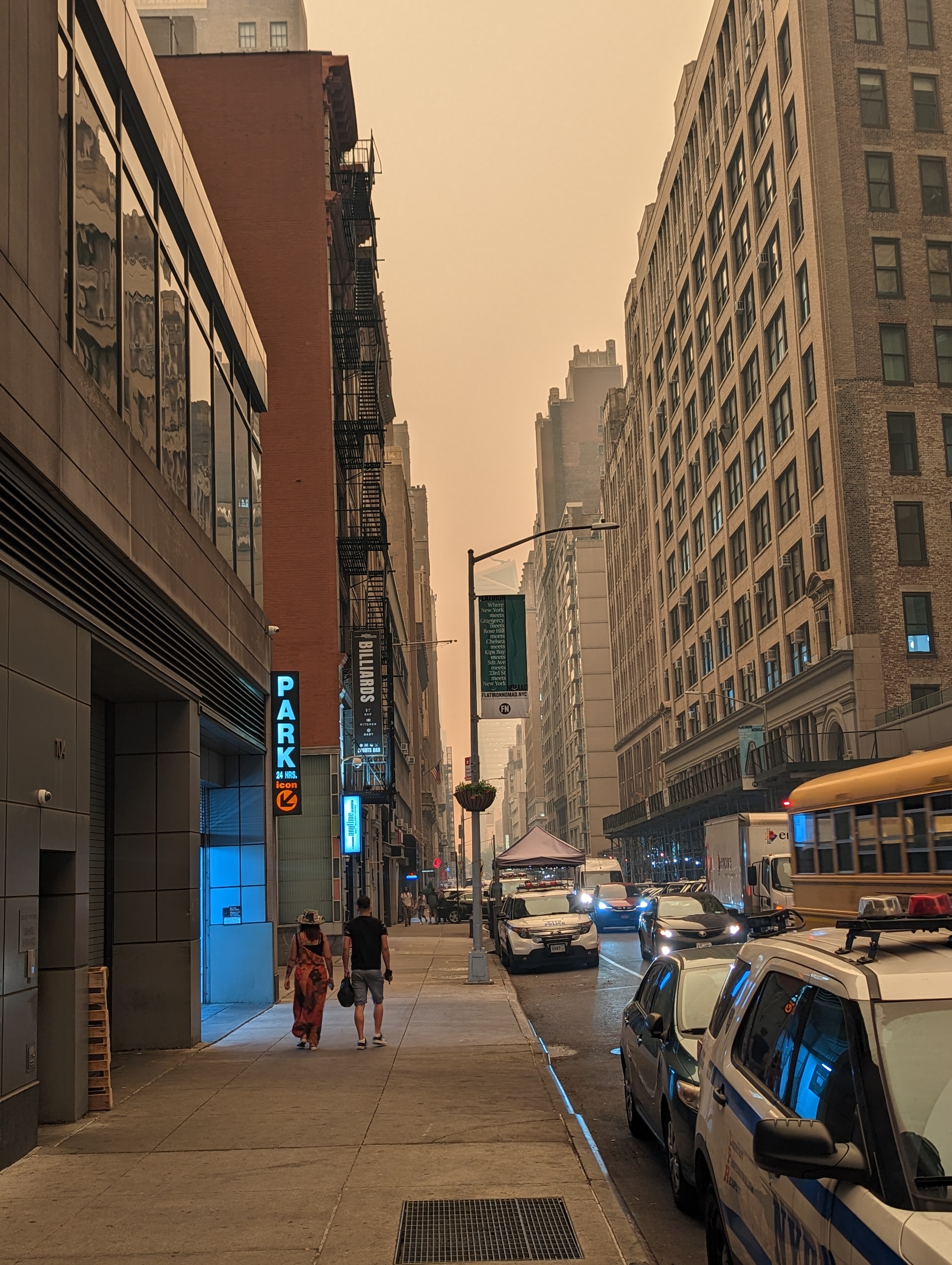 Pedestrians walk along a city street beneath thick orange wildfire smoke haze.