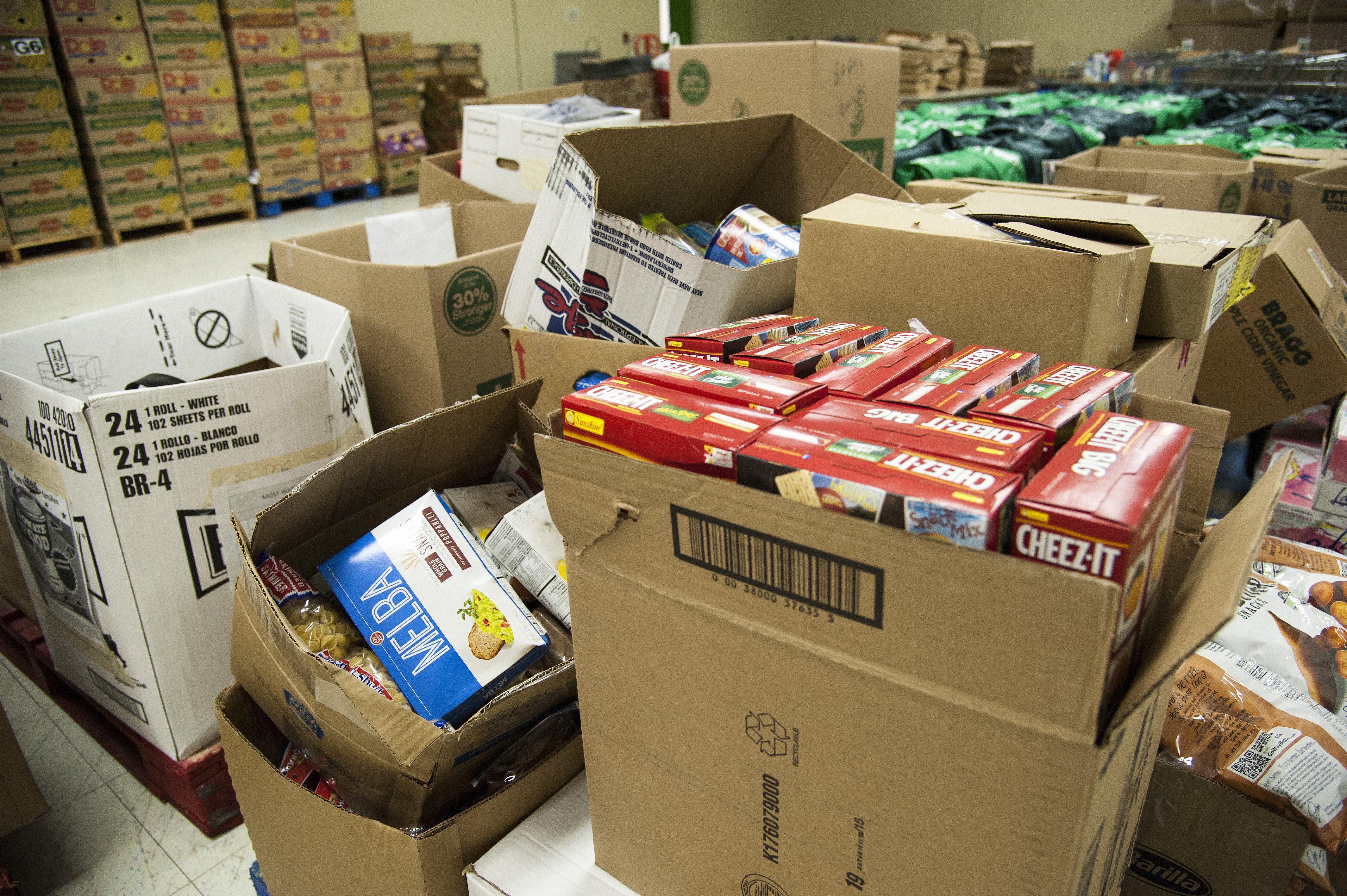 Stacked cardboard boxes filled with donated canned goods and packaged food in a pantry storage area.