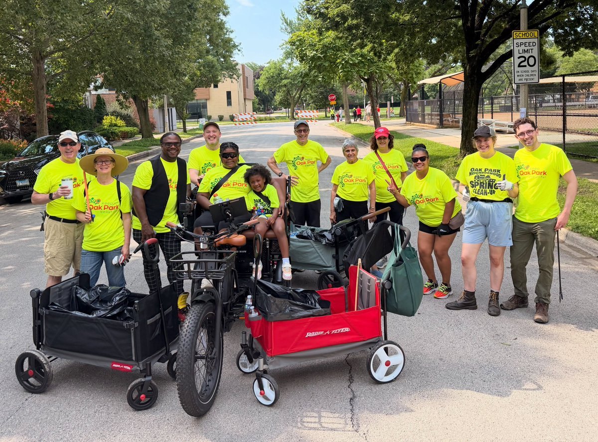 A group of volunteers in yellow t-shirts holding litter pickers and trash bags on a residential street.