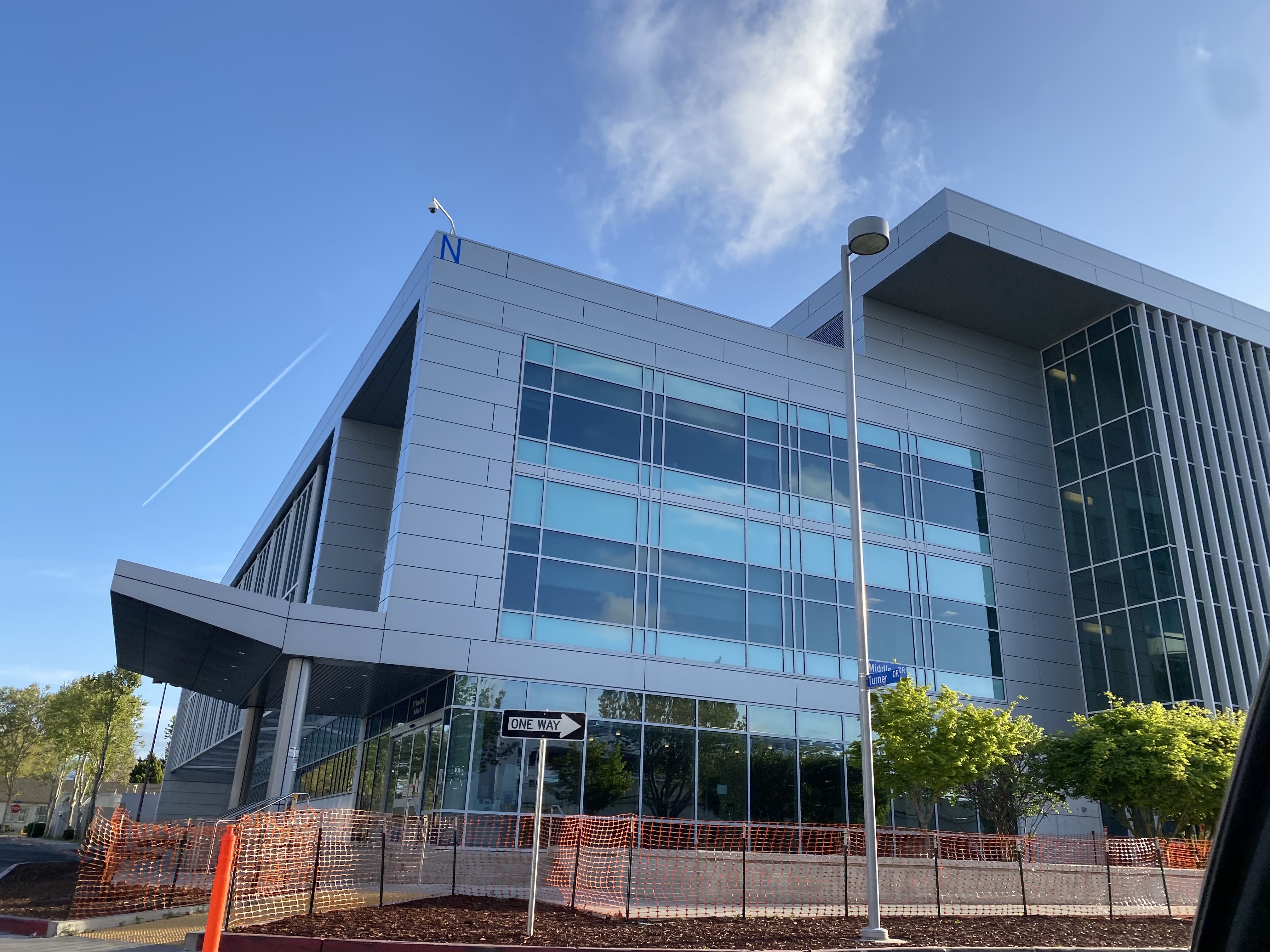 Multi-story glass and metal hospital building exterior with construction fencing along the perimeter