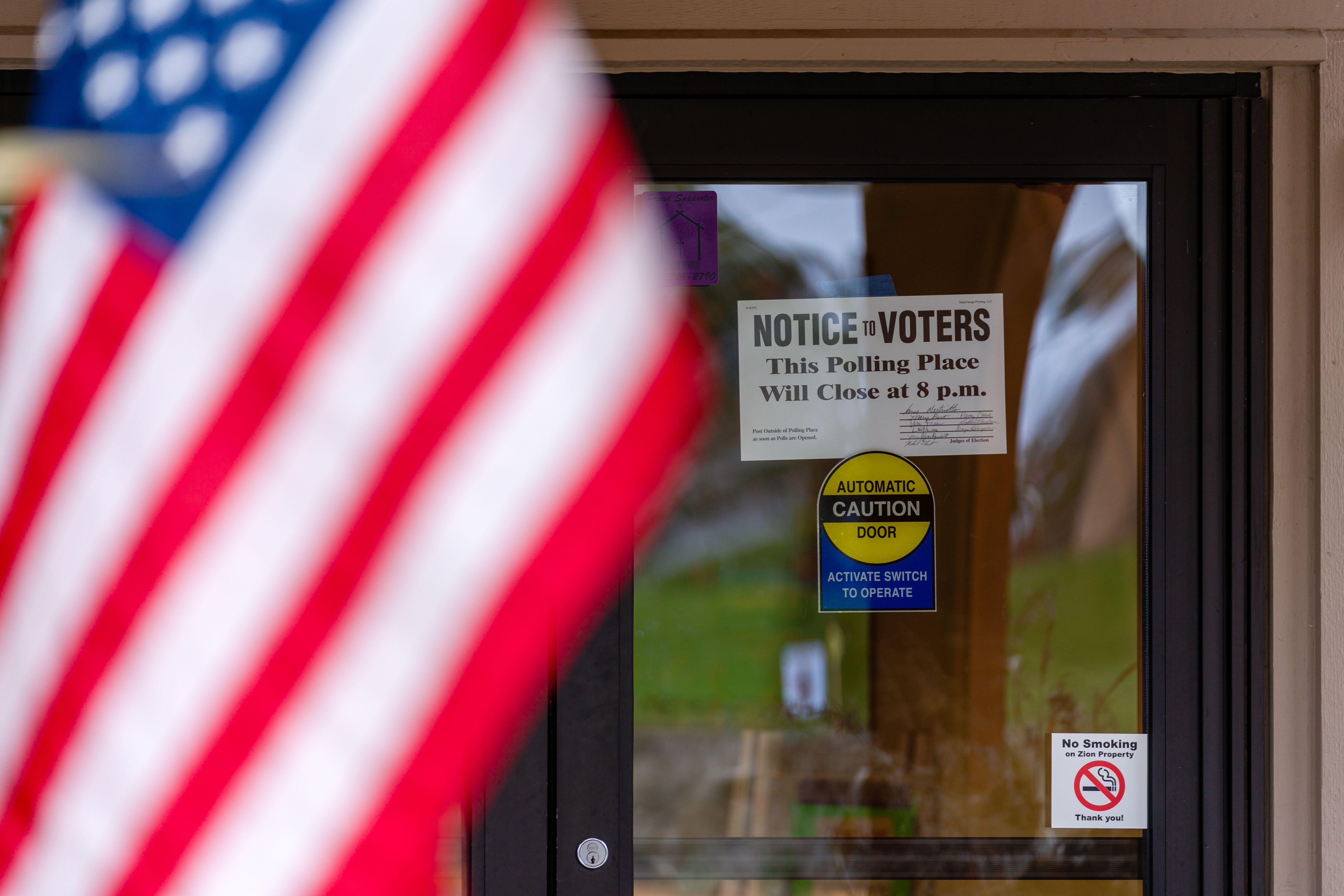 Glass door of a polling place with a voter notice sign and American flag.