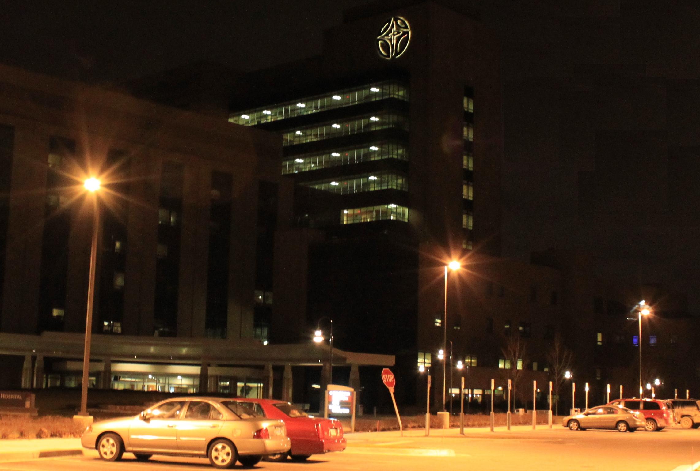 Hospital building at night with lit windows and an illuminated circular emblem on the upper facade.