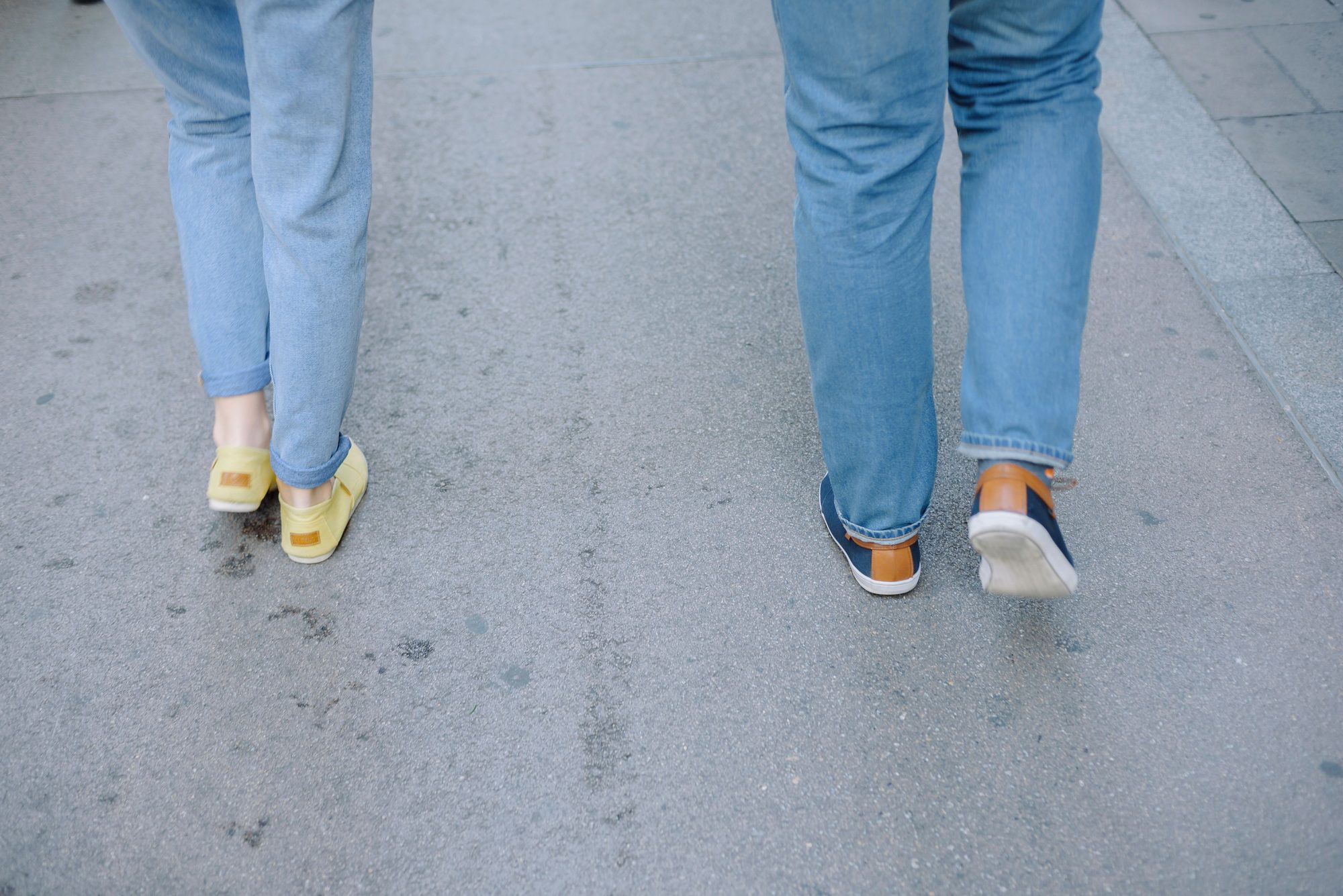 Two people walking casually on a city pavement in jeans and sneakers.