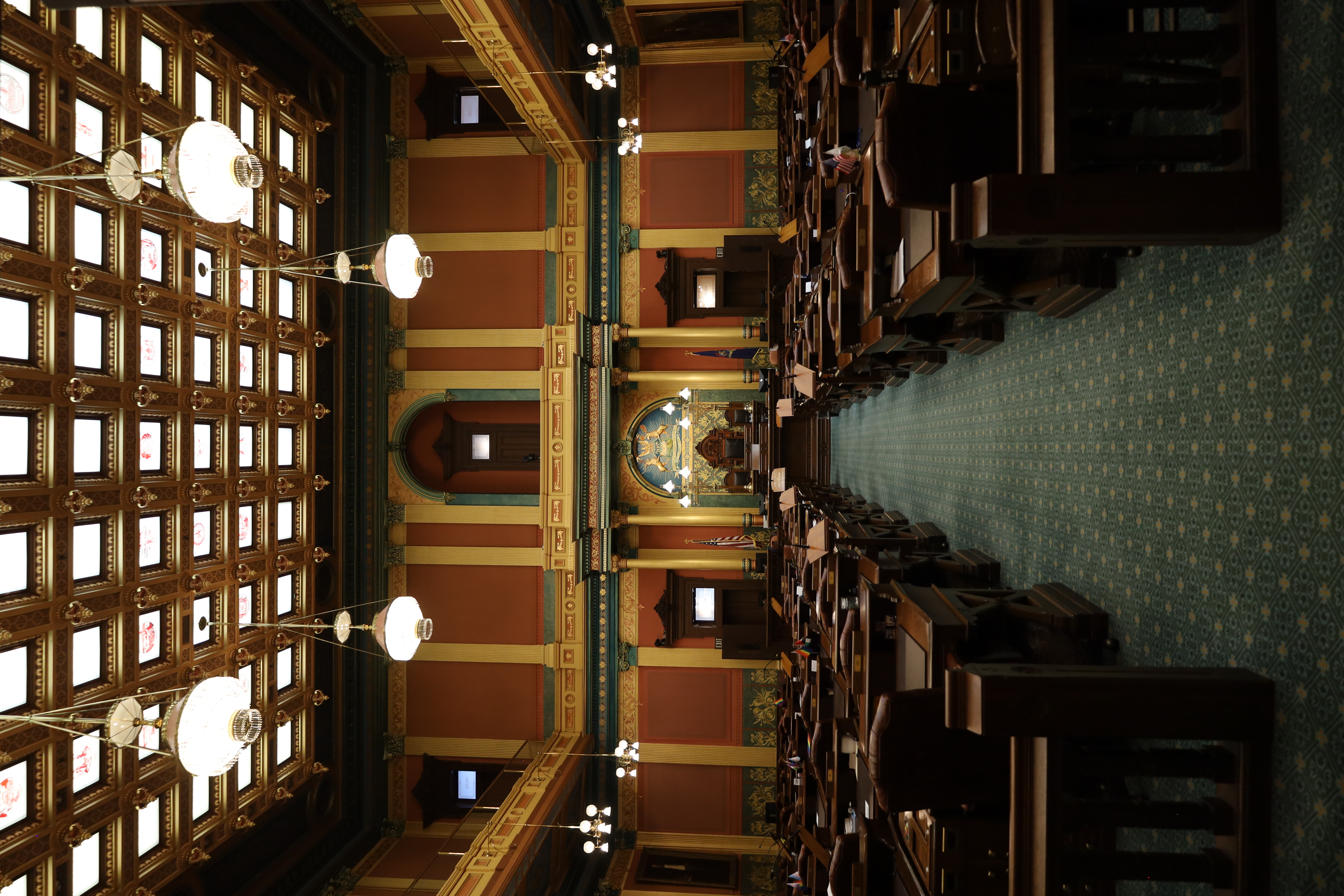Legislative chamber with rows of wooden desks, skylights, and a raised speaker's dais.